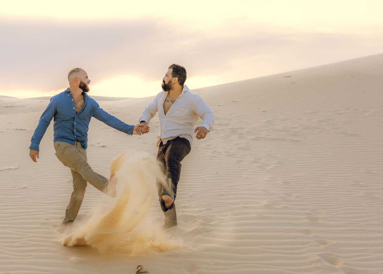 People running and kicking up sand on desert dunes during golden hour.