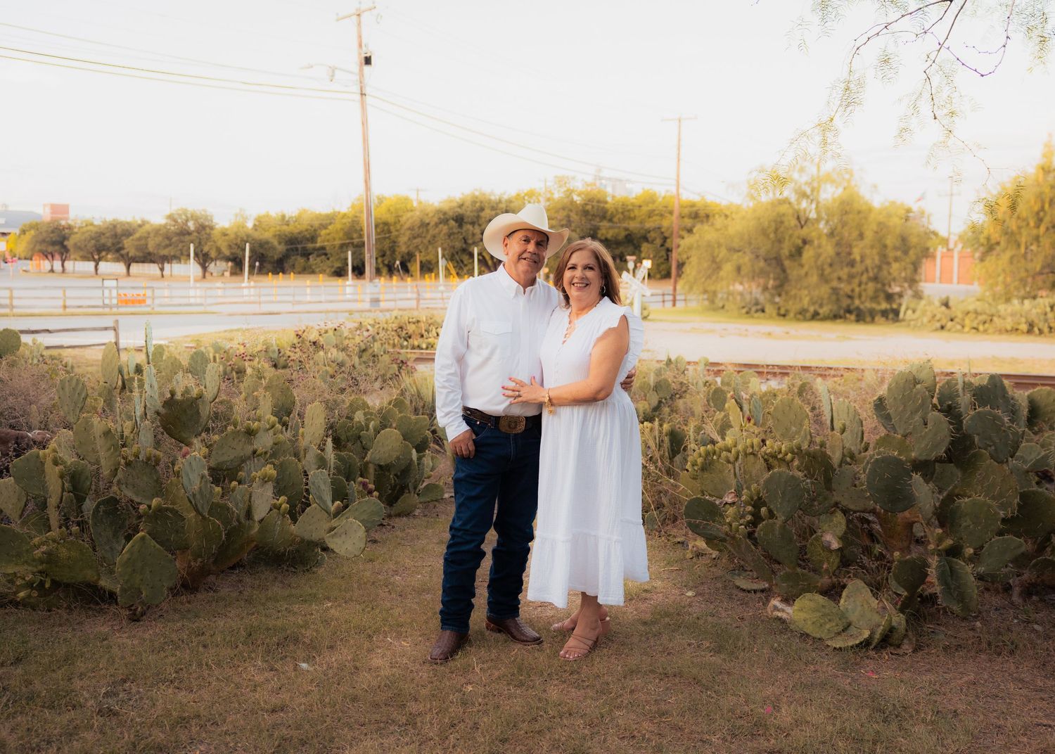 A couple dances and poses in a natural desert setting with cacti and brush.