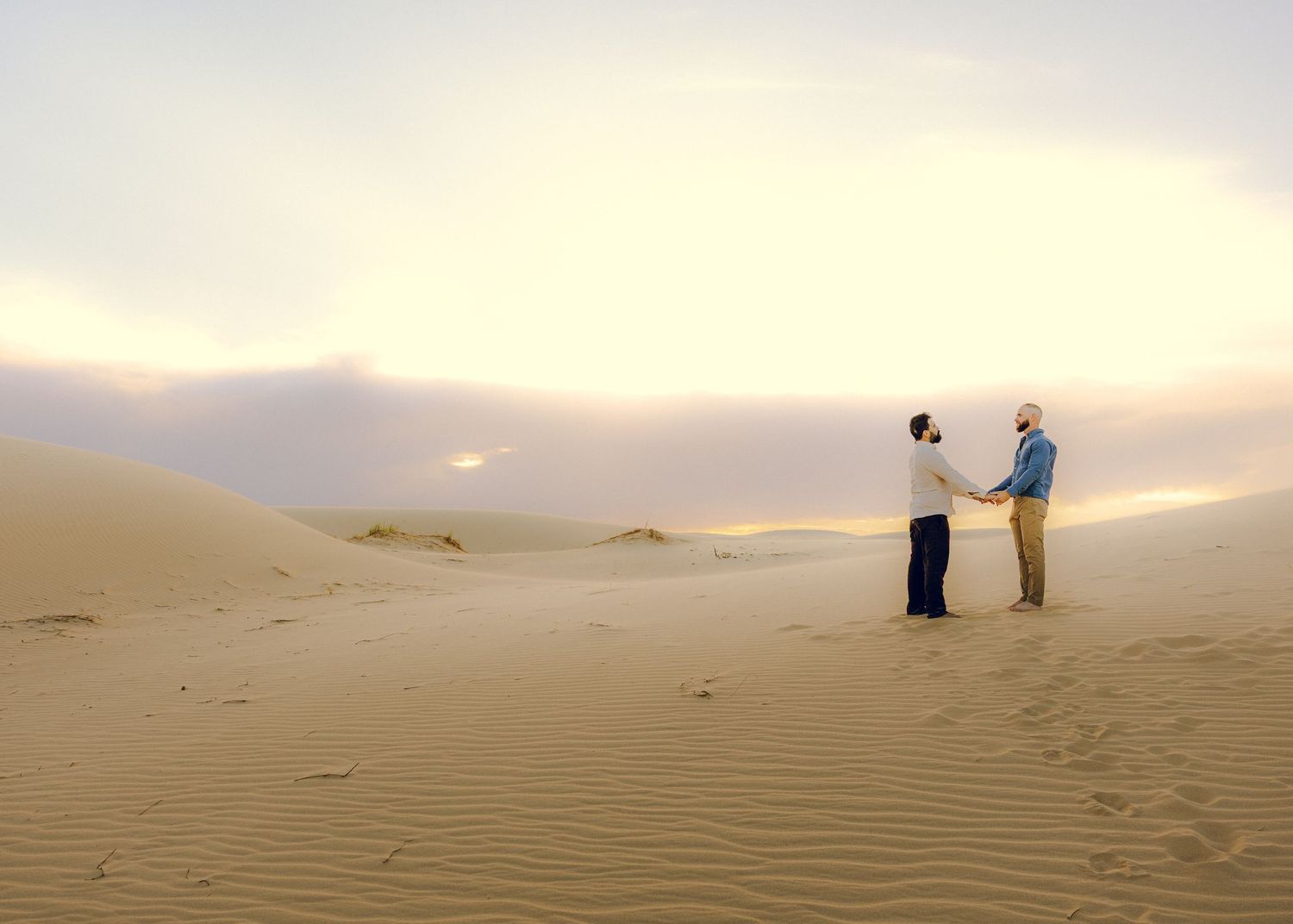 Photographers working in vast desert sand dunes during sunset.