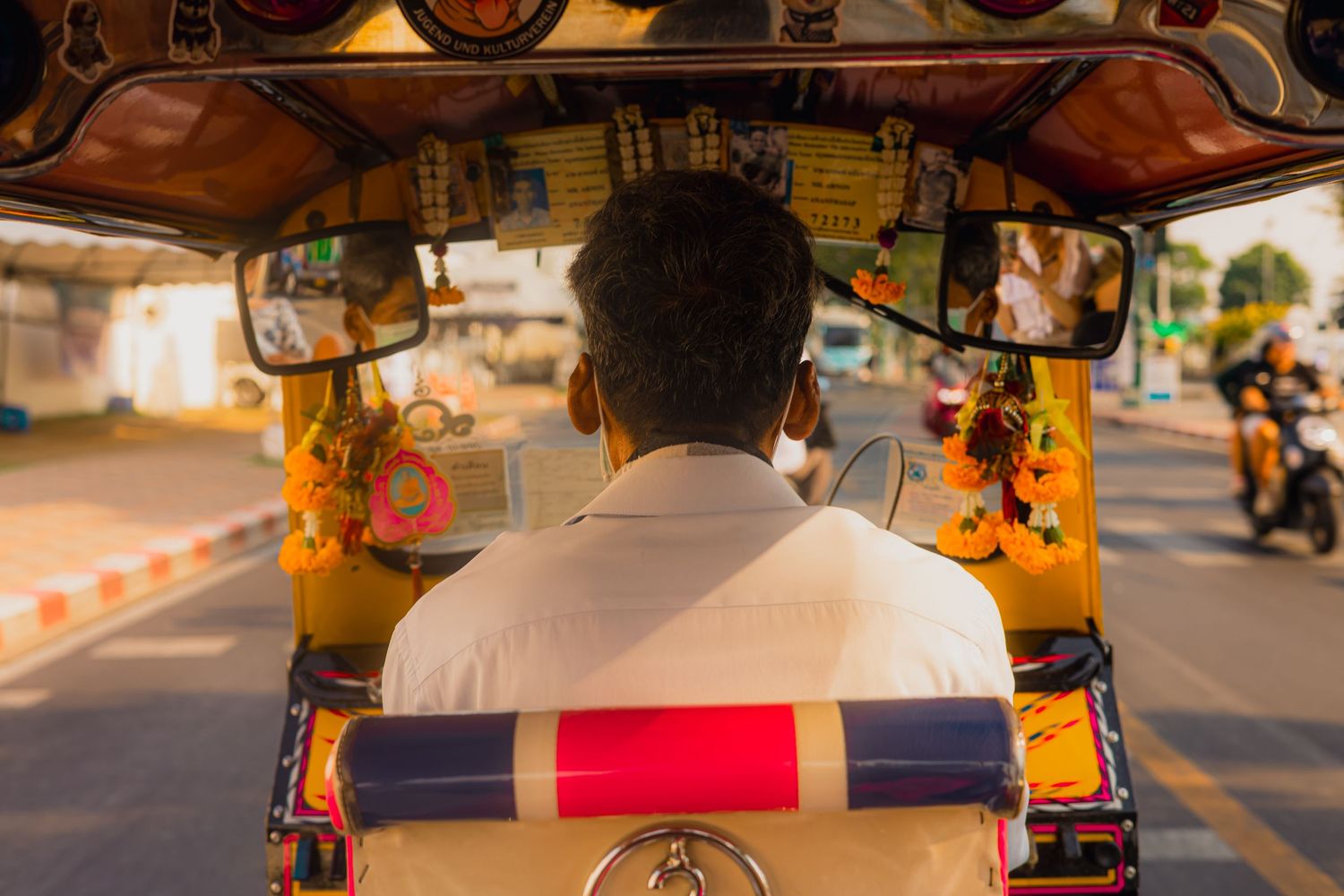 Rear view of a tuk-tuk driver navigating a busy Thai street in a traditional three-wheeled vehicle.
