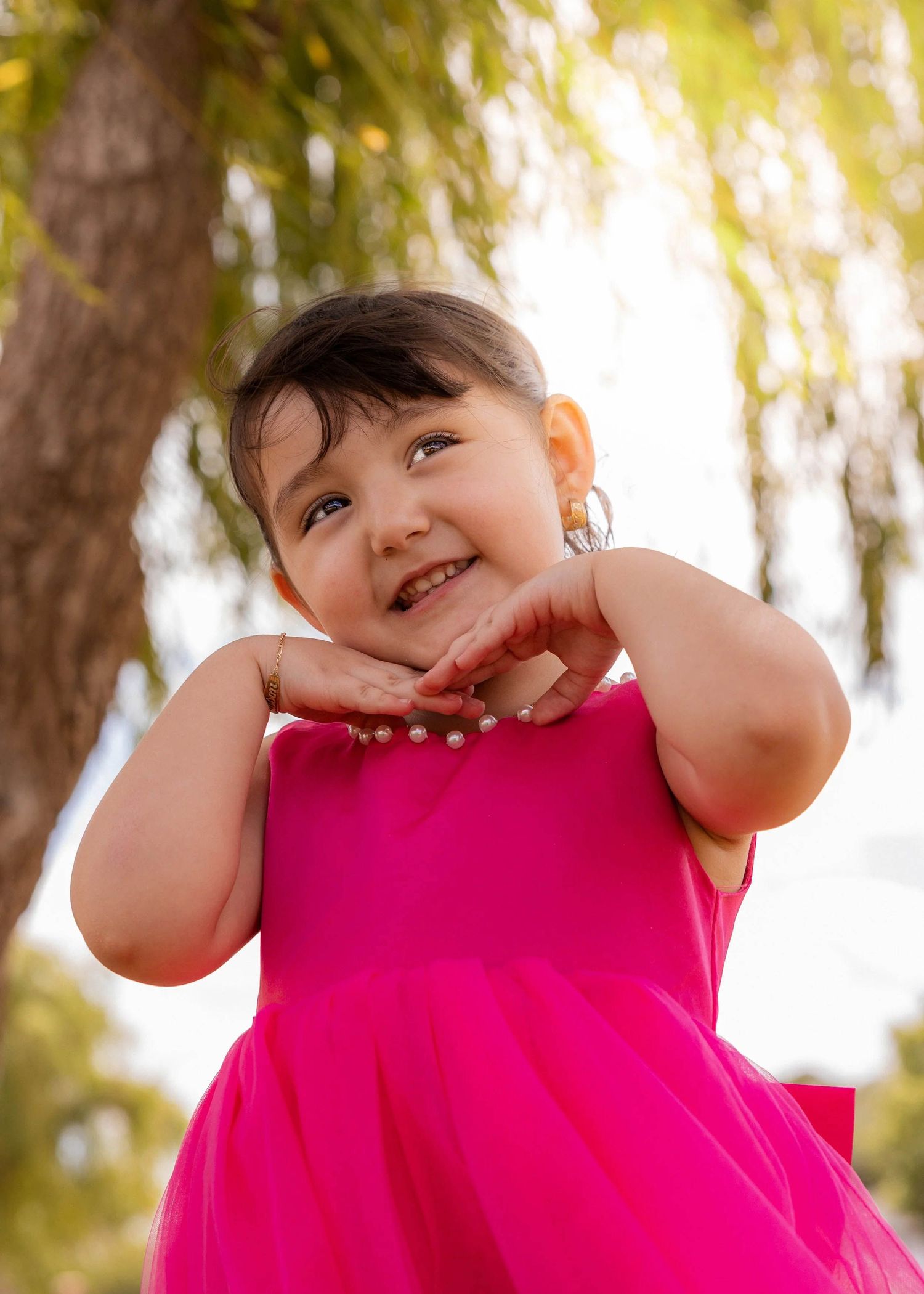 Child in pink dress making playful expressions in outdoor setting.