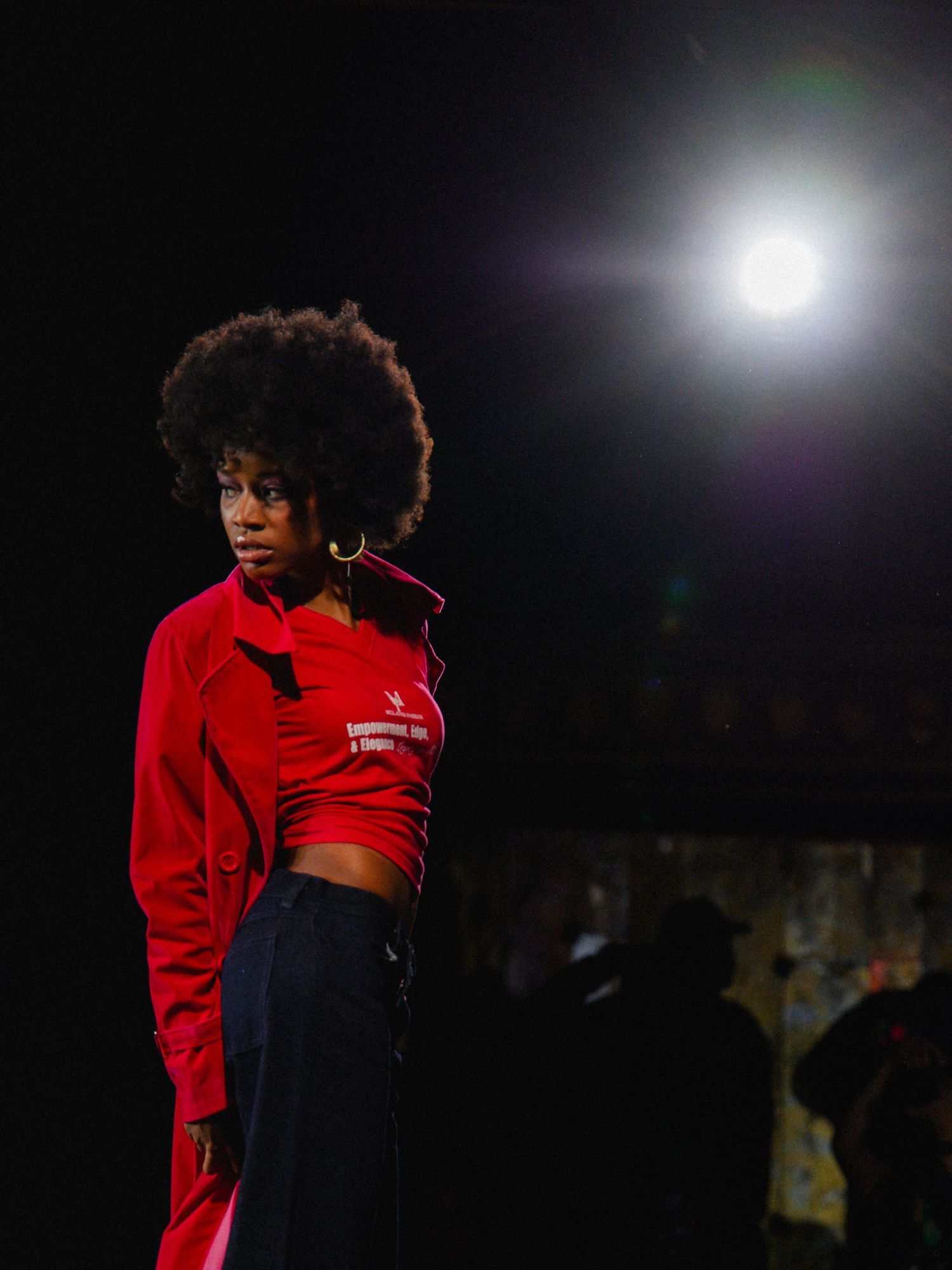 A dancer in a red crop top performs a dynamic movement sequence against a dark background with dramatic lighting.