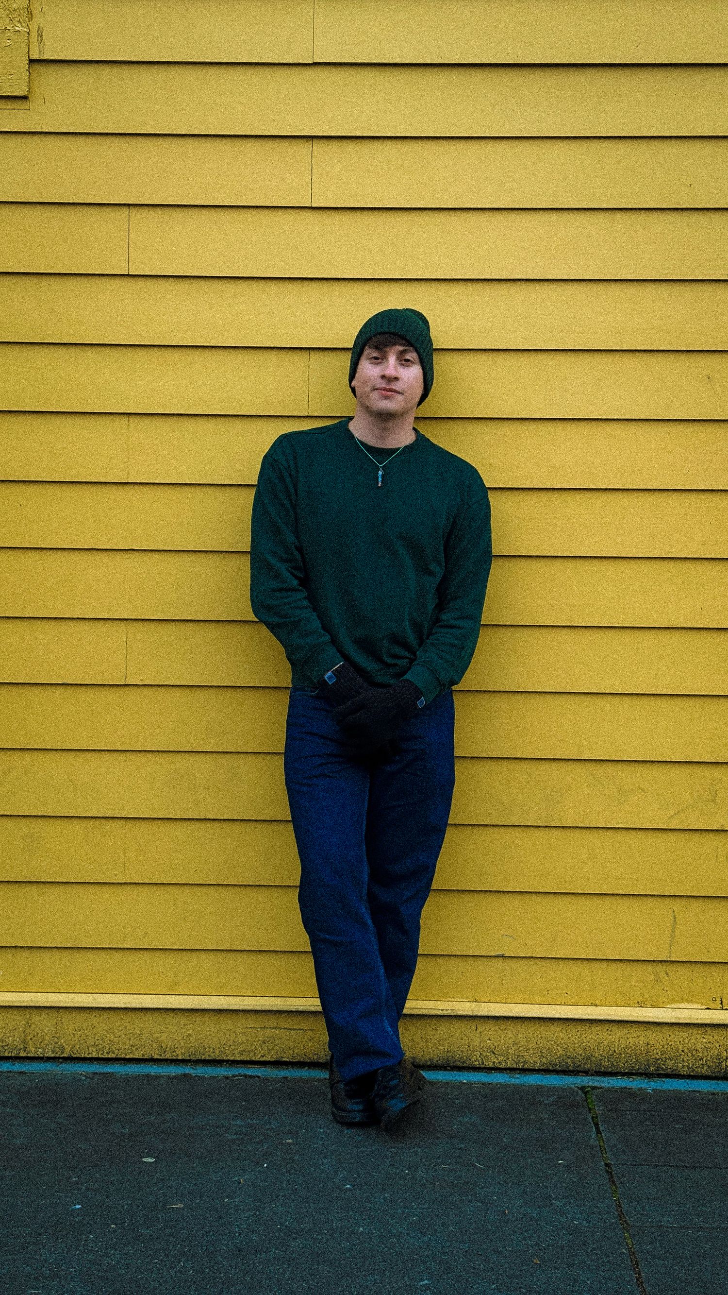 Person in dark clothing sits against bright yellow wall creating stark visual contrast.
