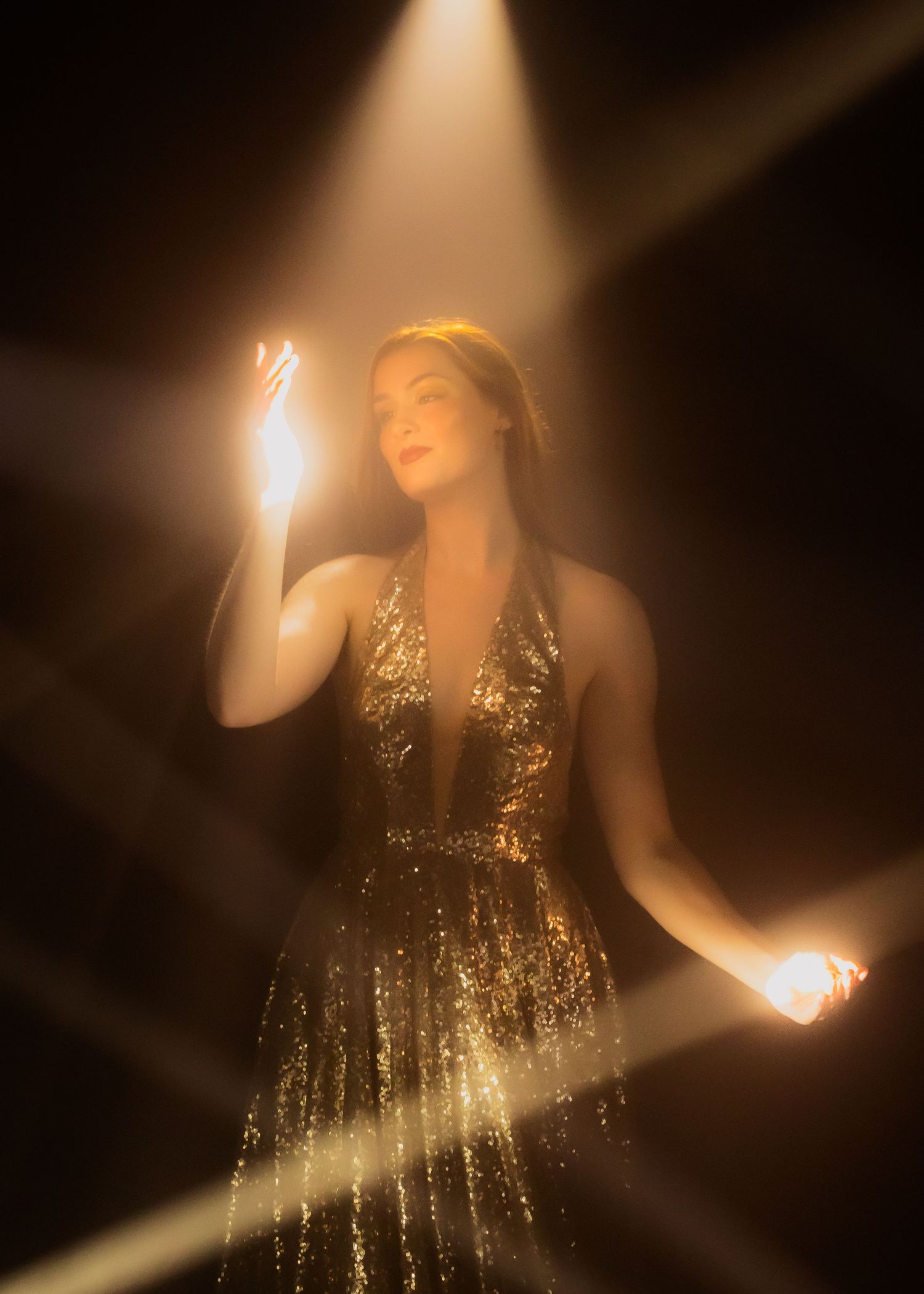 Dramatic lighting illuminates a figure in a sequined dress against a dark background.