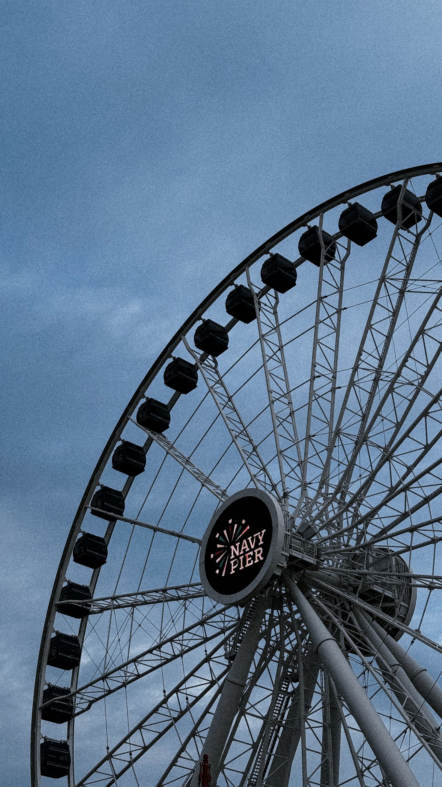 Dramatic silhouette of a large Ferris wheel against a moody blue sky.