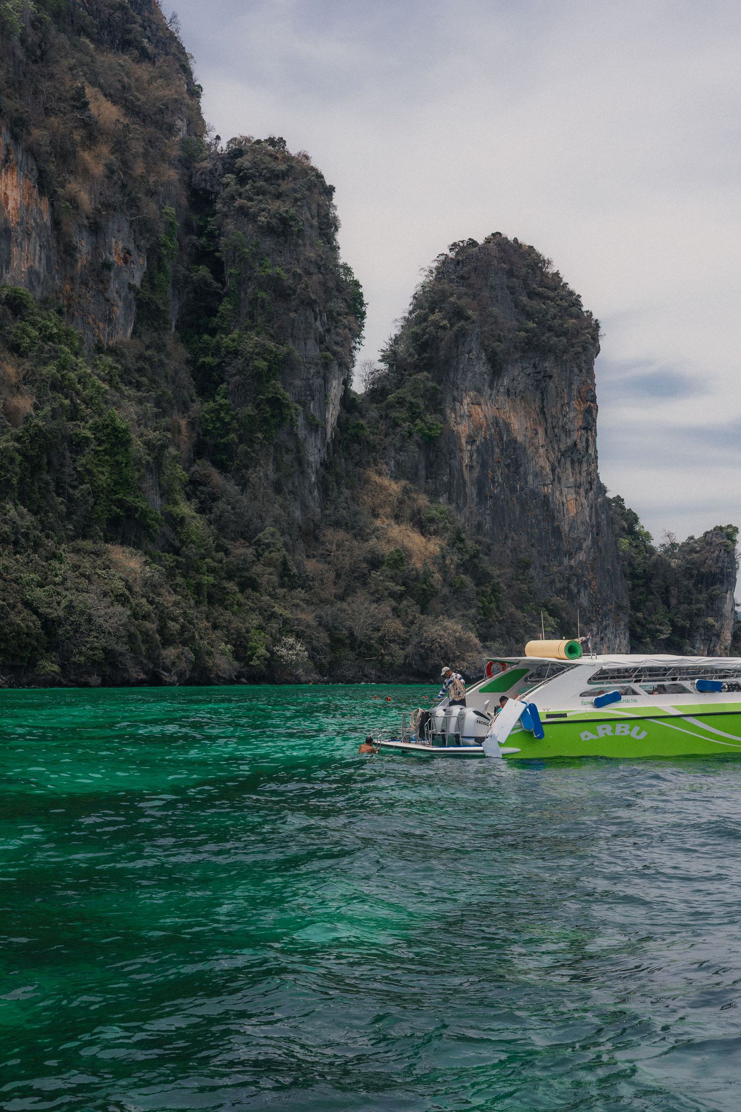 Green speedboat near dramatic limestone cliffs in emerald waters, Krabi Thailand island hopping tour.
