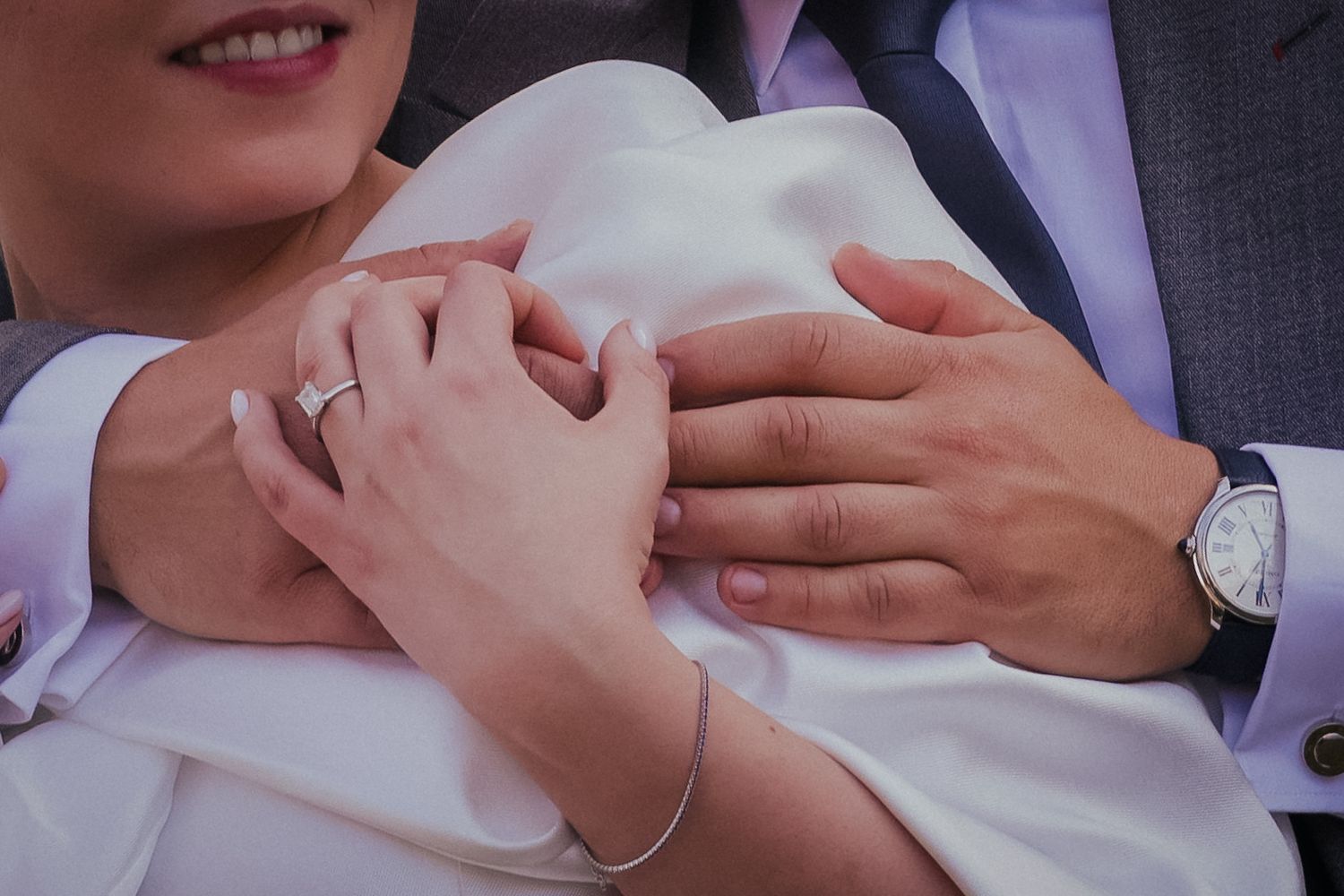 Close-up shot of wedding rings and hands embracing in formal attire.