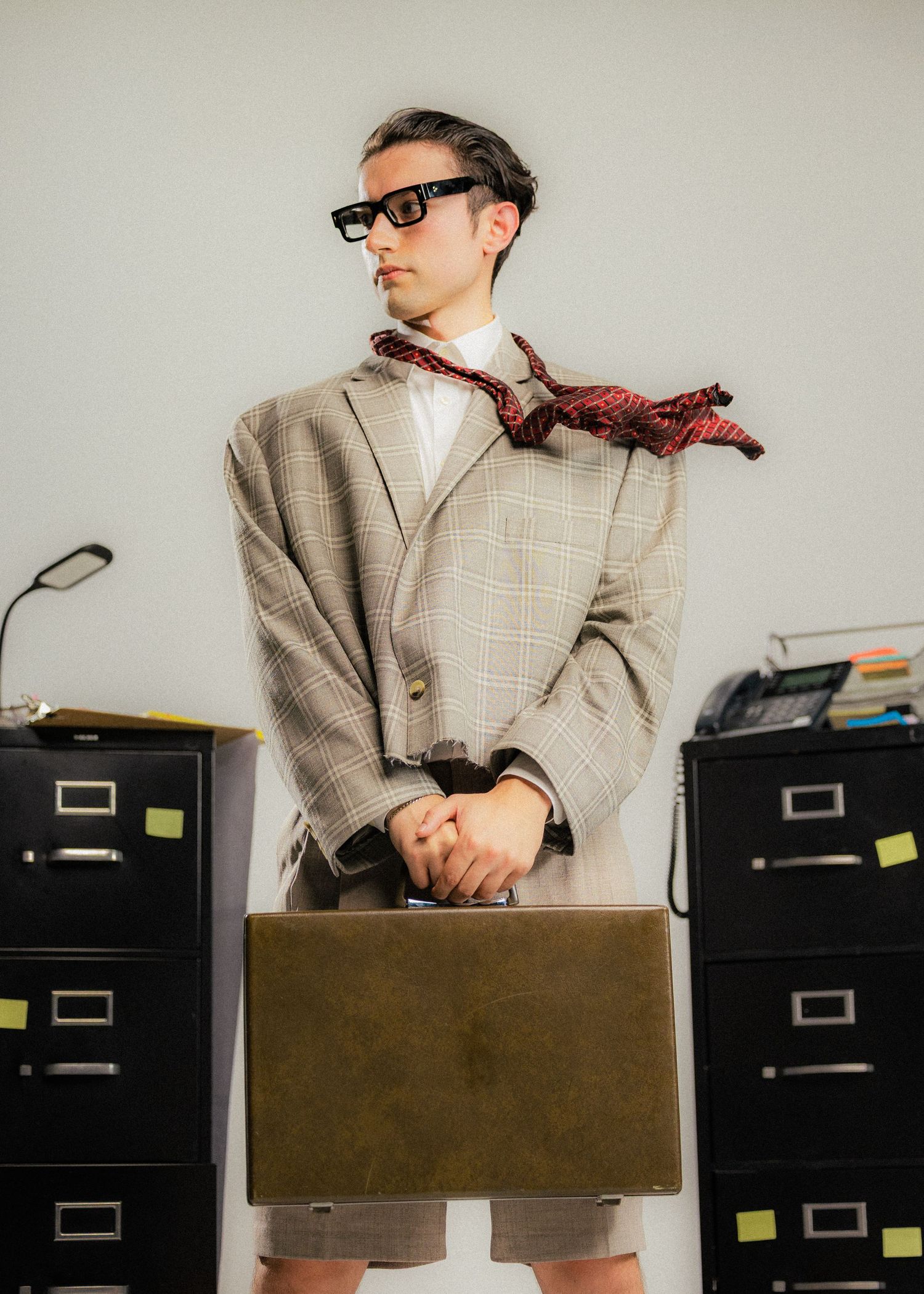 Person in plaid suit posing with briefcase near office filing cabinets.