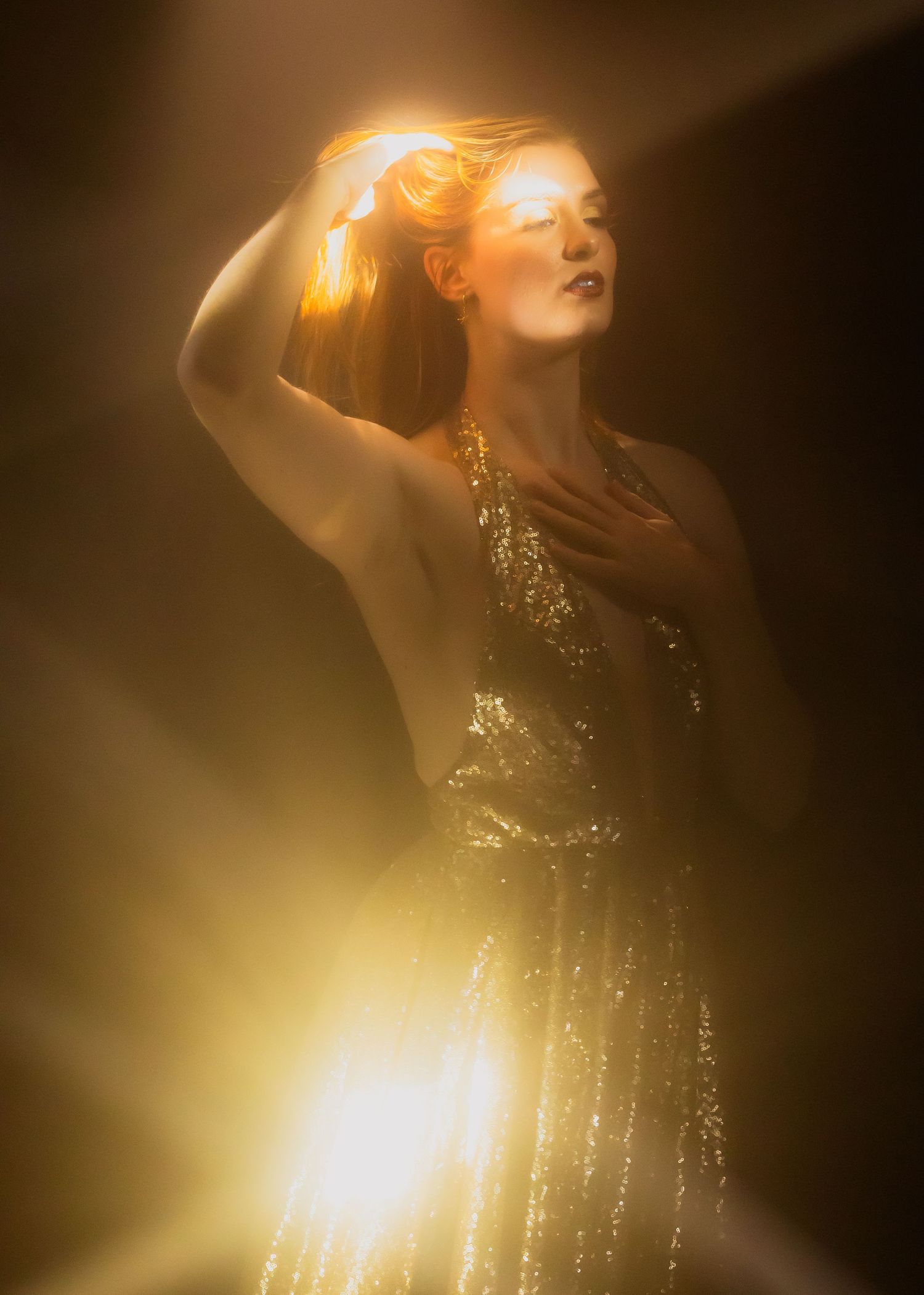 Ethereal golden-lit portrait features sparkly dress and graceful pose against dark background.