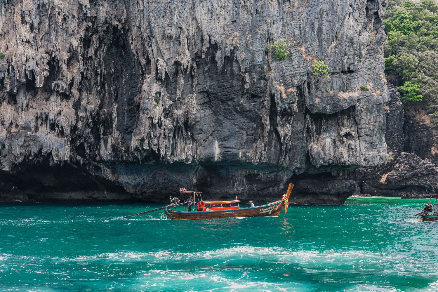 A traditional Thai longtail boat floating on turquoise waters near dramatic limestone cliffs in Thailand.