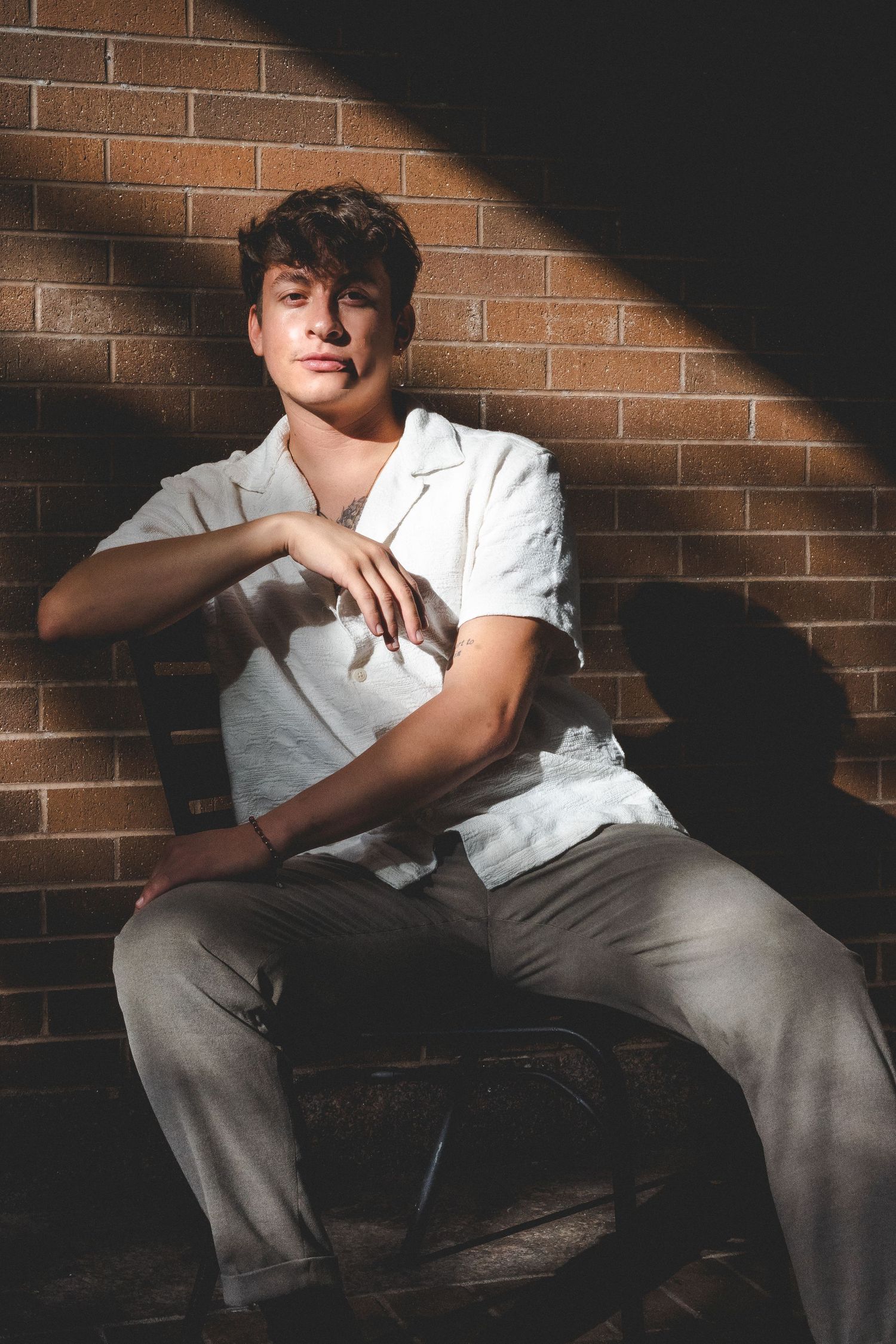 Dramatic portrait with strong shadows against brick wall background.