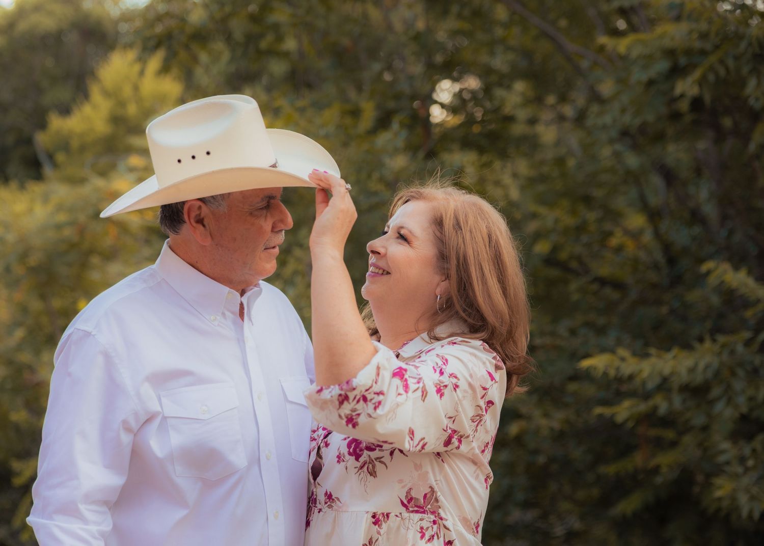 Couple in white and floral outfits sharing tender moment outdoors.