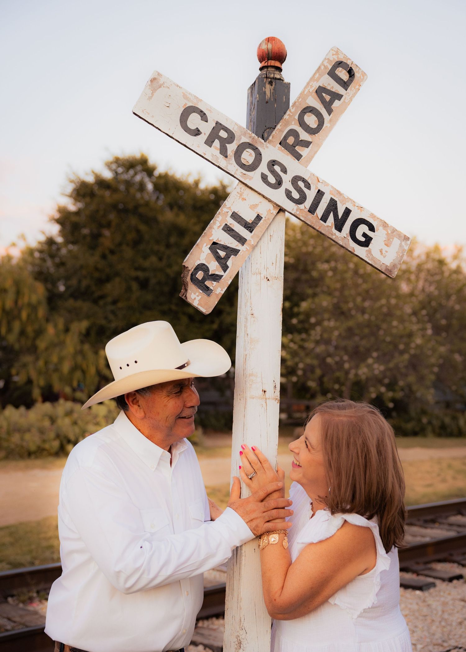 A romantic photoshoot by a railroad crossing sign creates unique engagement portraits.