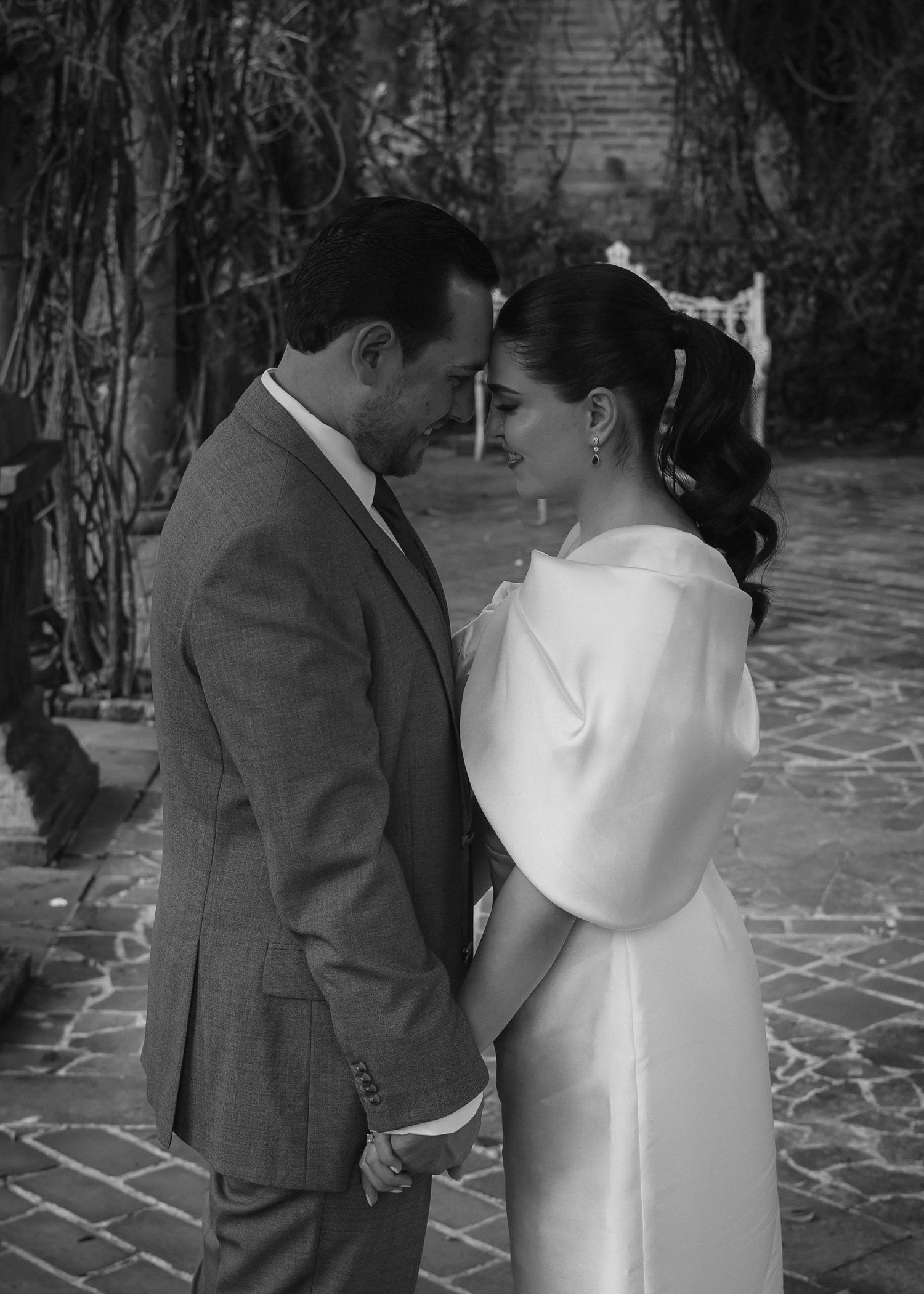 Black and white portrait of a couple sharing an intimate moment under garden vines.