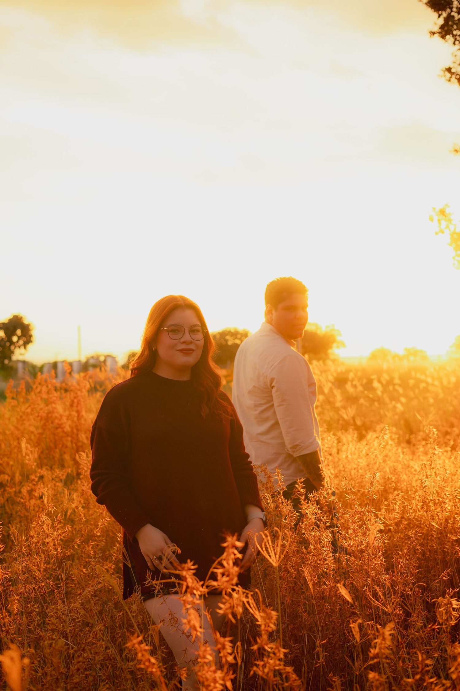 Two people standing in a golden field at sunset with warm glowing light creating a dreamy autumn atmosphere.