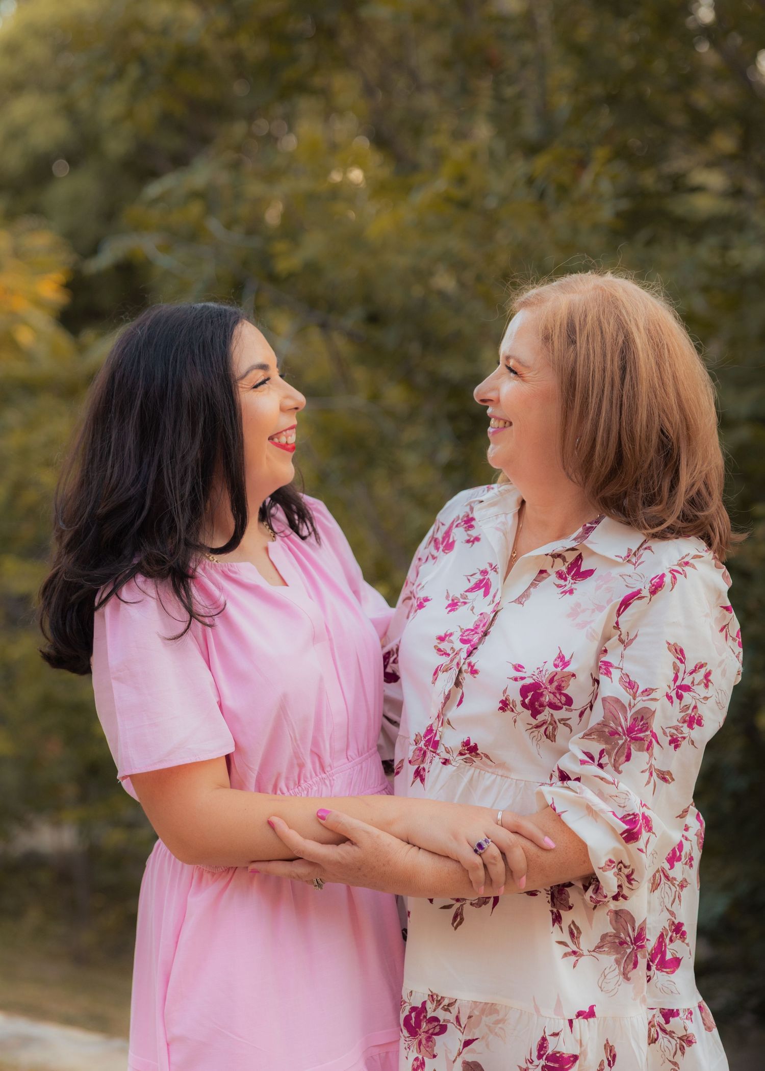 Two people in pink and floral outfits share joyful laughter during a photo session.
