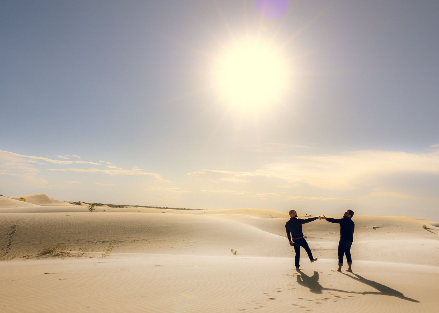 Silhouettes of people walking and posing on sand dunes at sunset.