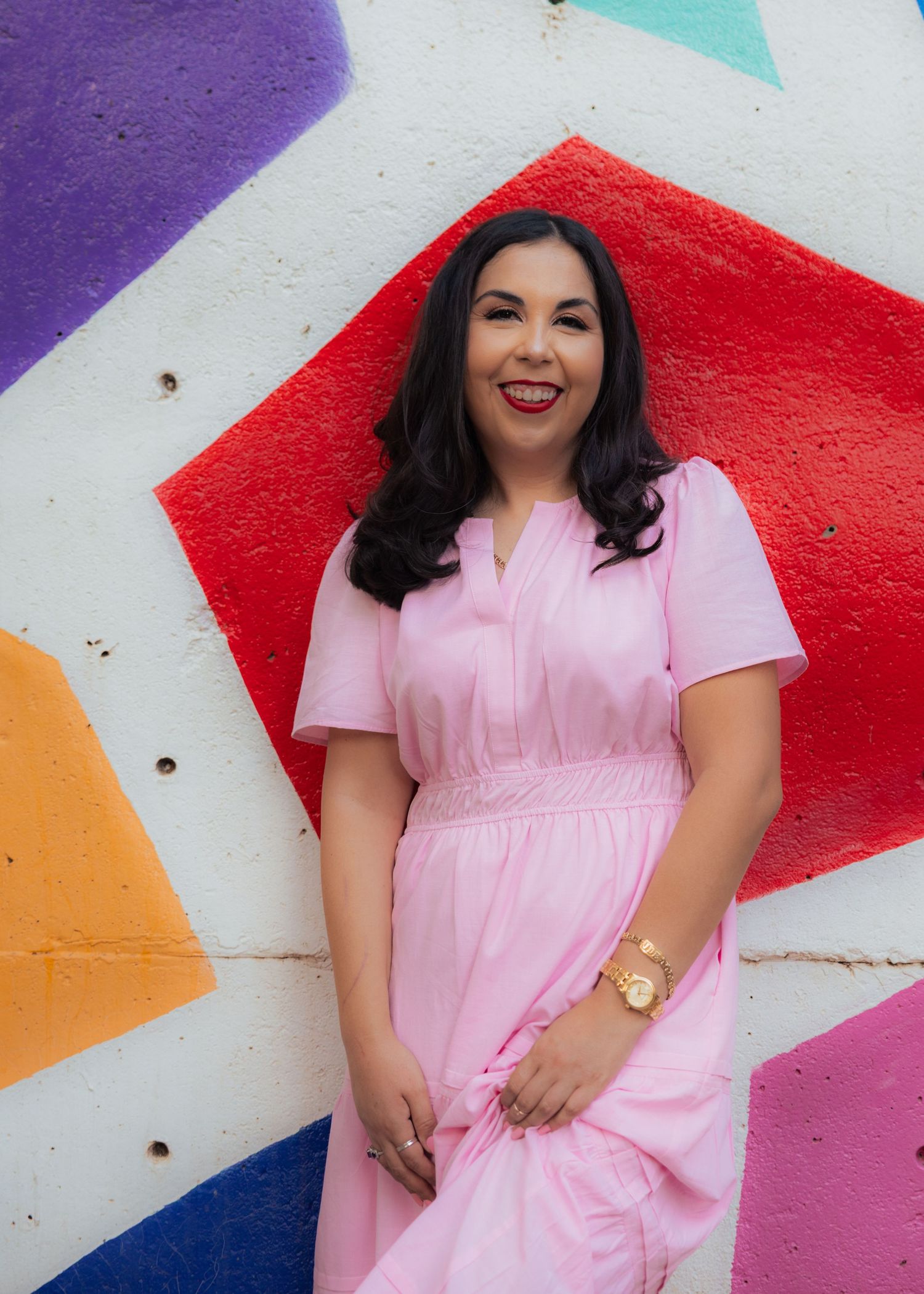 Person in pink dress poses against colorful geometric wall mural.