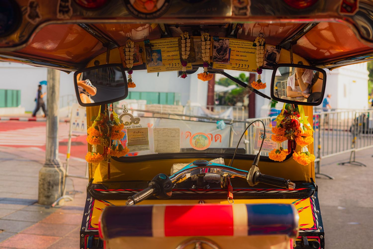 Interior view of a colorful Thai tuk-tuk with decorations, mirrors, and dashboard ornaments parked on a street.