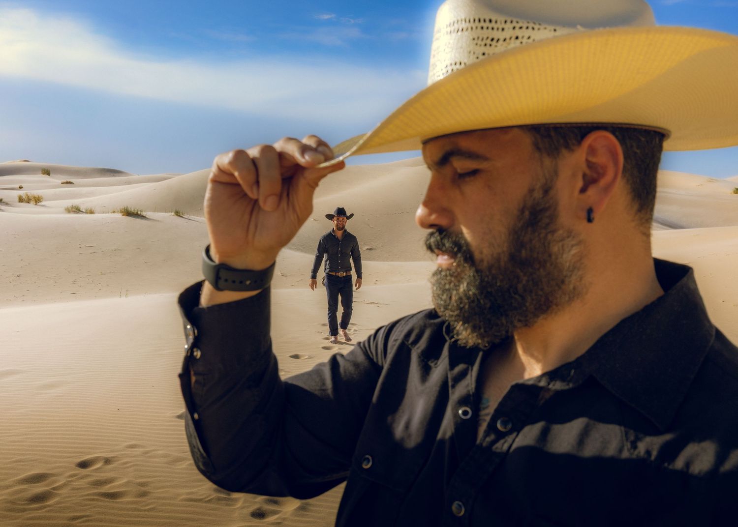 Person in cowboy hat poses in desert landscape while another figure walks in background.