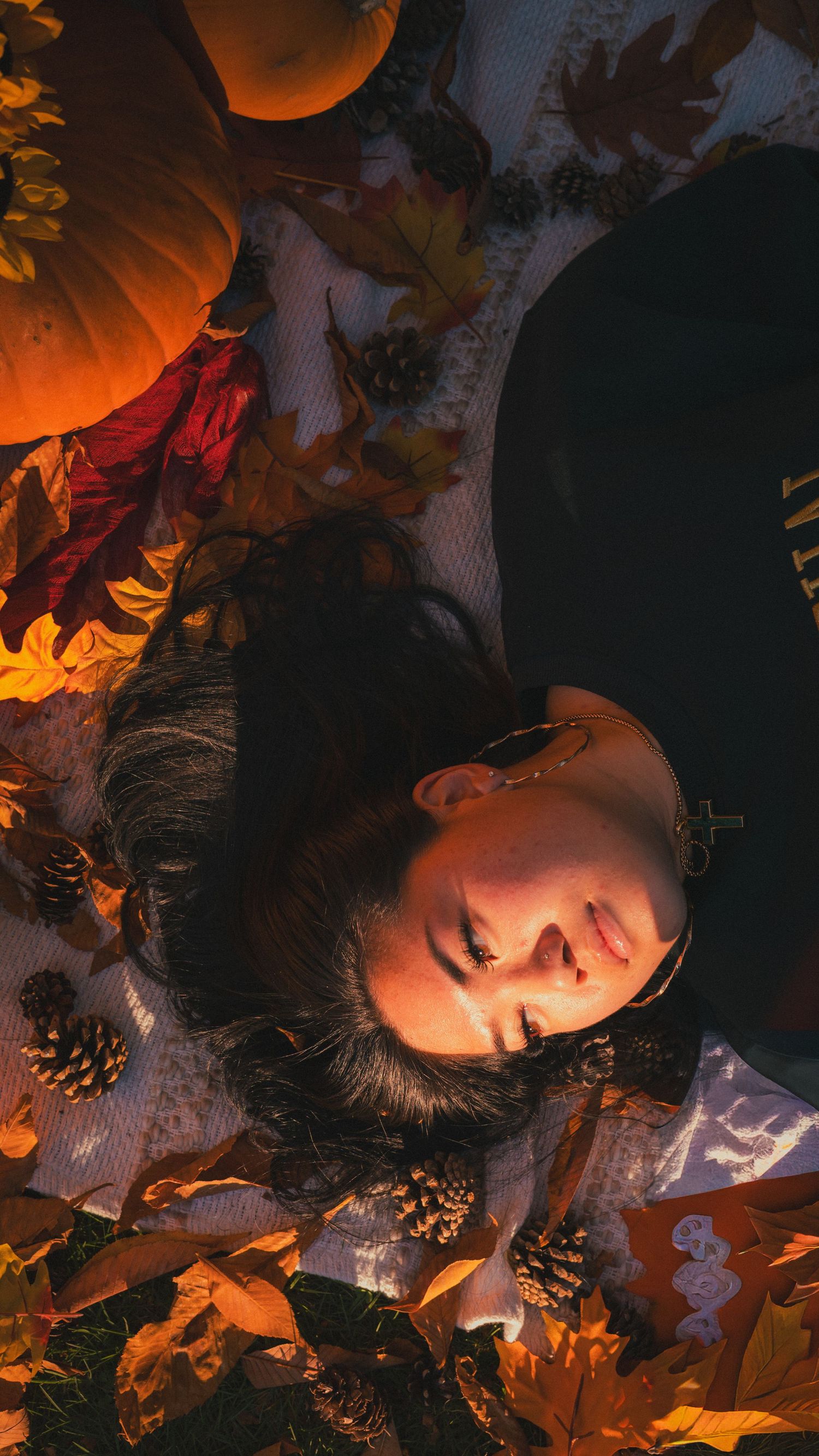 Artistic autumn portrait with orange leaves and dramatic lighting creating a moody atmosphere.