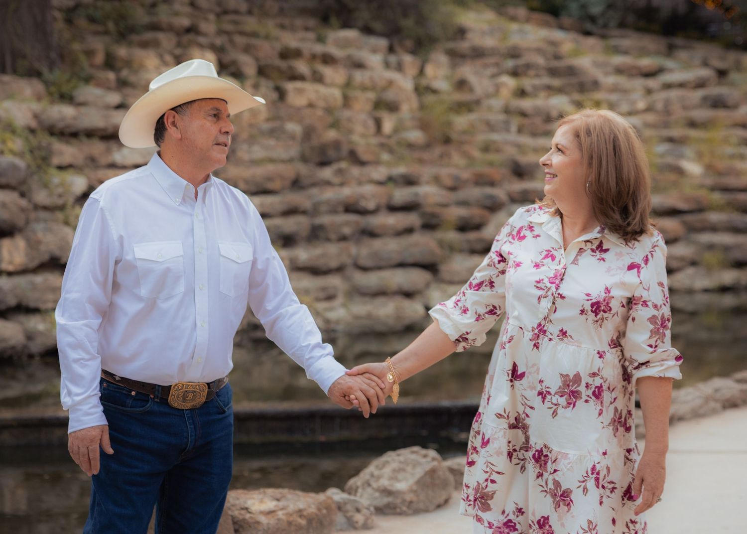 A couple shares a tender moment at sunset near a stone wall in a romantic outdoor photoshoot.