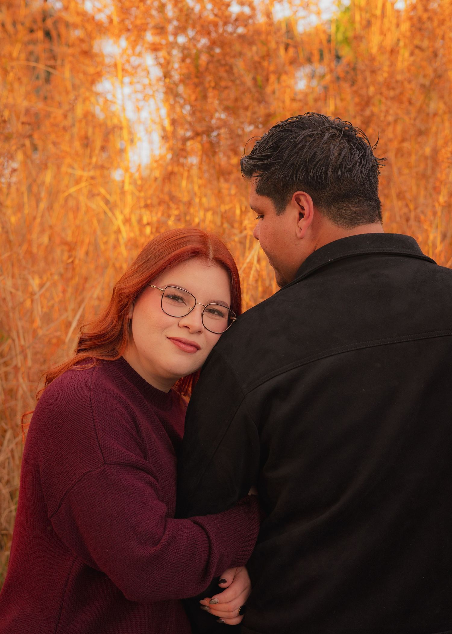 A couple shares a romantic moment against a backdrop of vibrant orange autumn foliage in a forest setting.