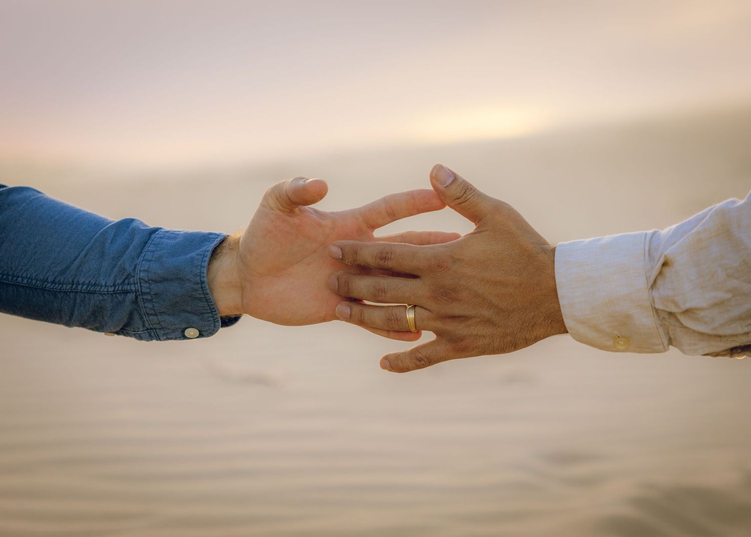 Sequence of hands reaching across sand dunes at sunset.