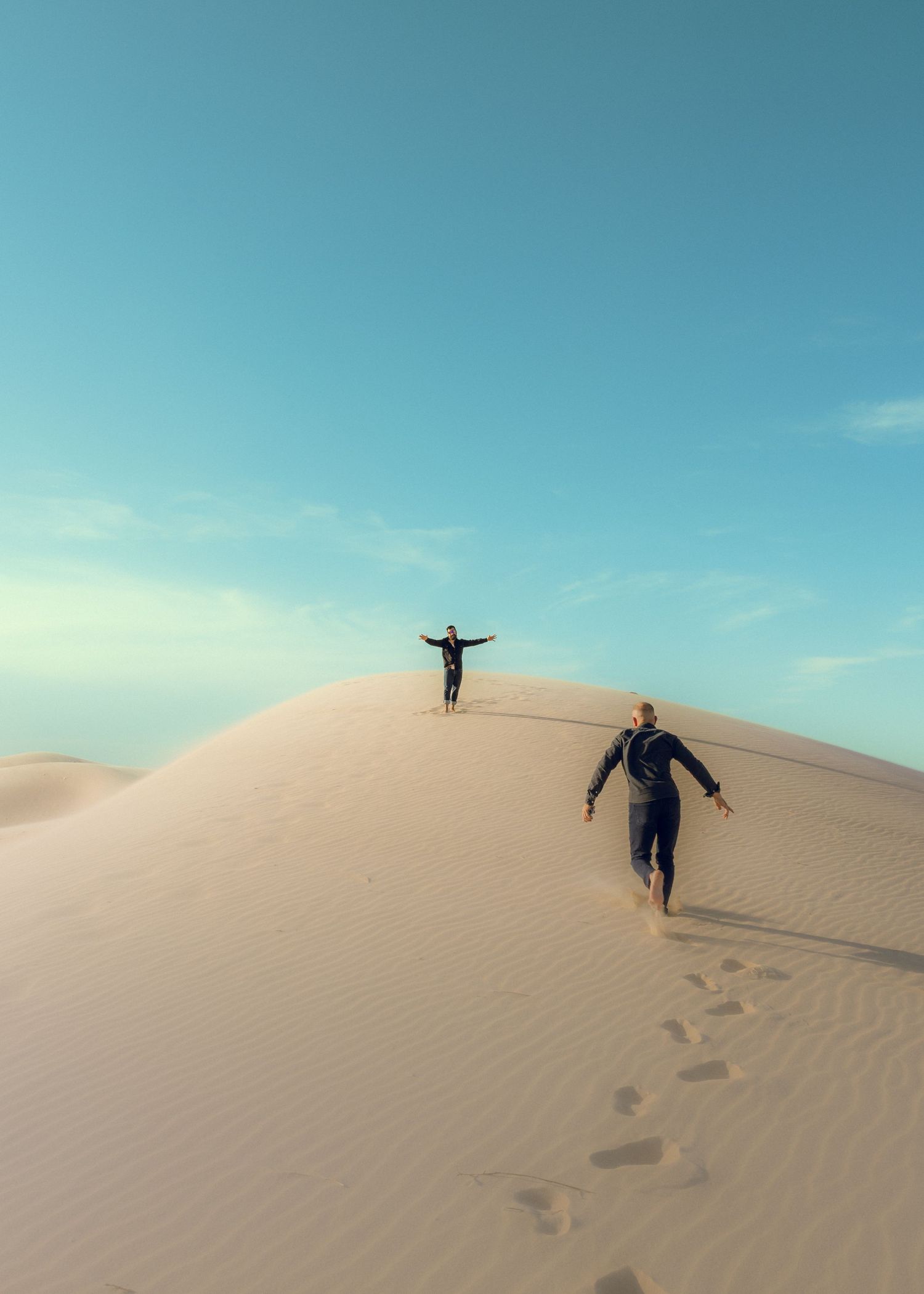 Person running and playing on sandy dunes against bright blue sky.