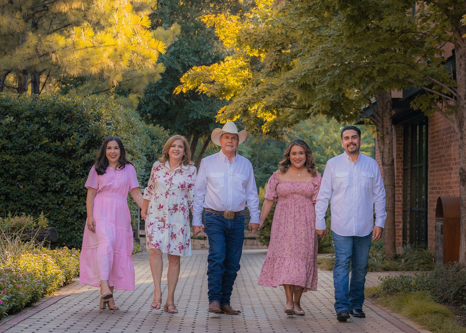 Group portrait of family members wearing pink and white outfits on brick pathway.