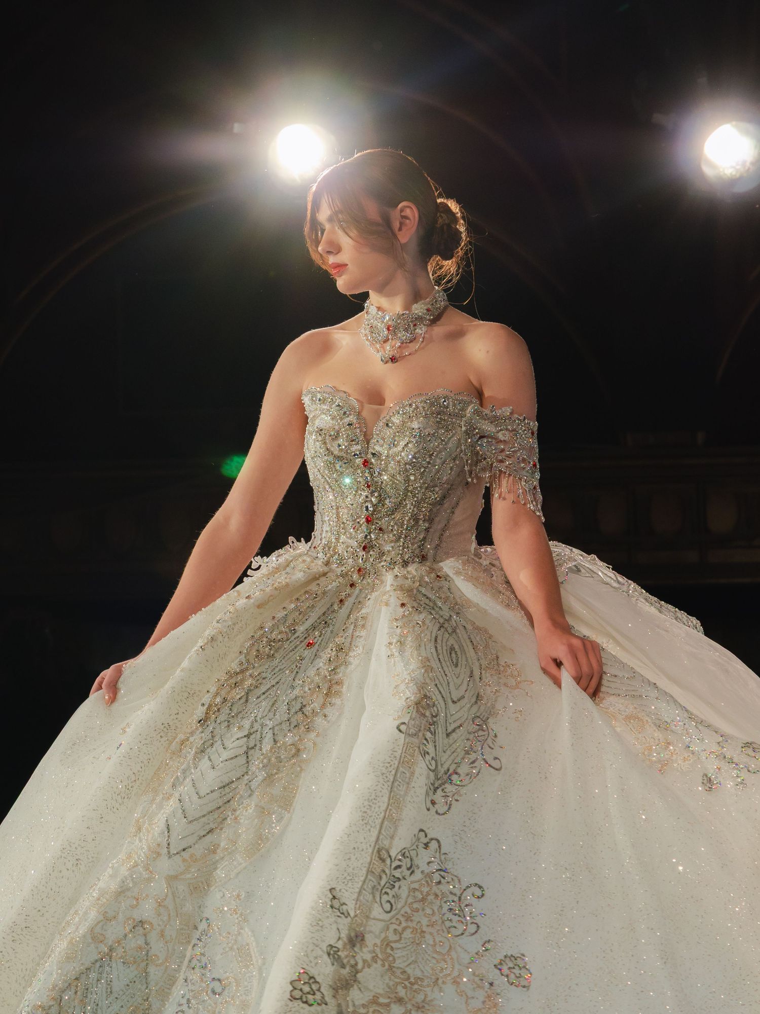 A stunning off-shoulder wedding gown with intricate beading and a voluminous tulle skirt sparkles under dramatic lighting.