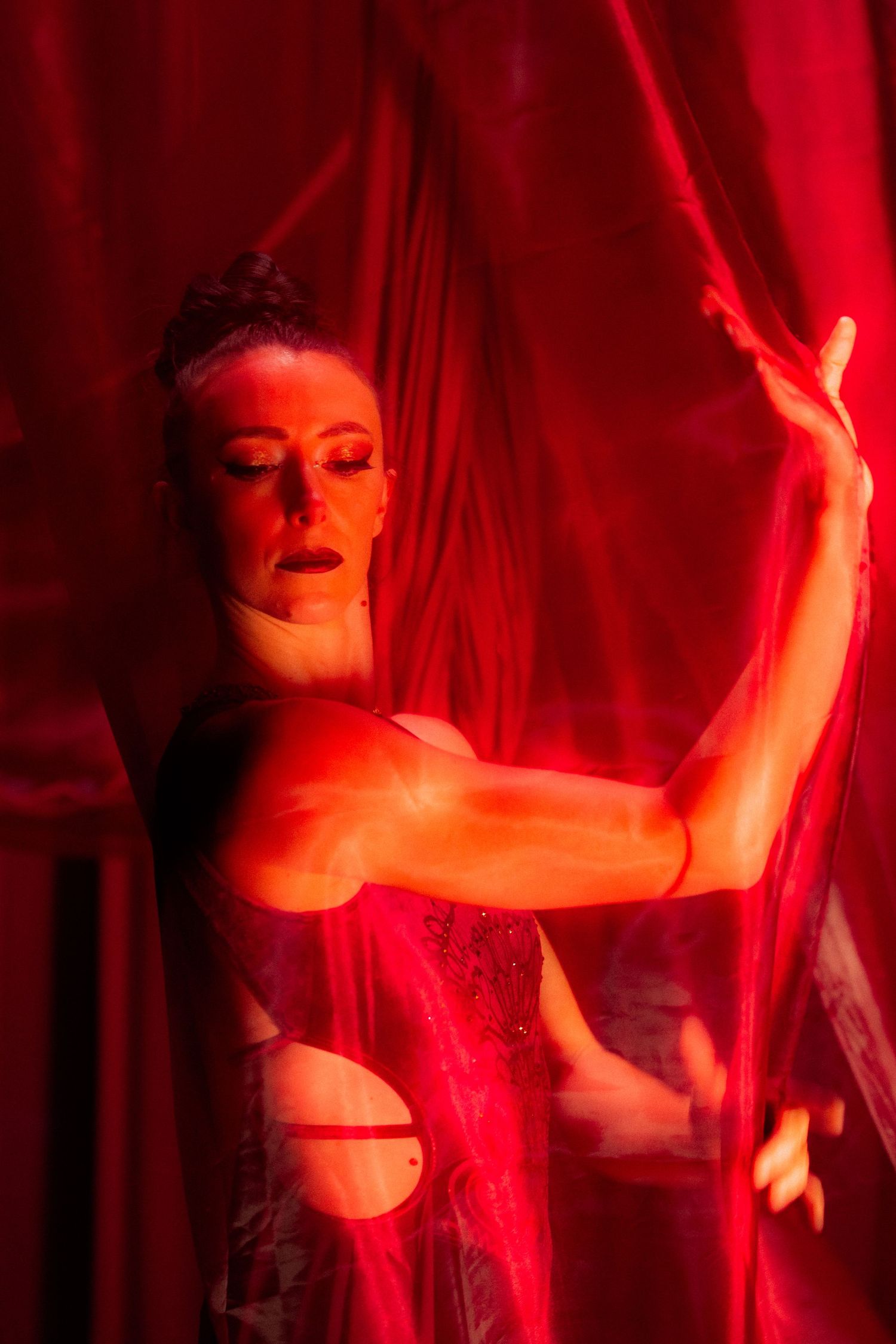Dancer in red sparkly costume performs against dramatic red curtain backdrop with theatrical lighting.