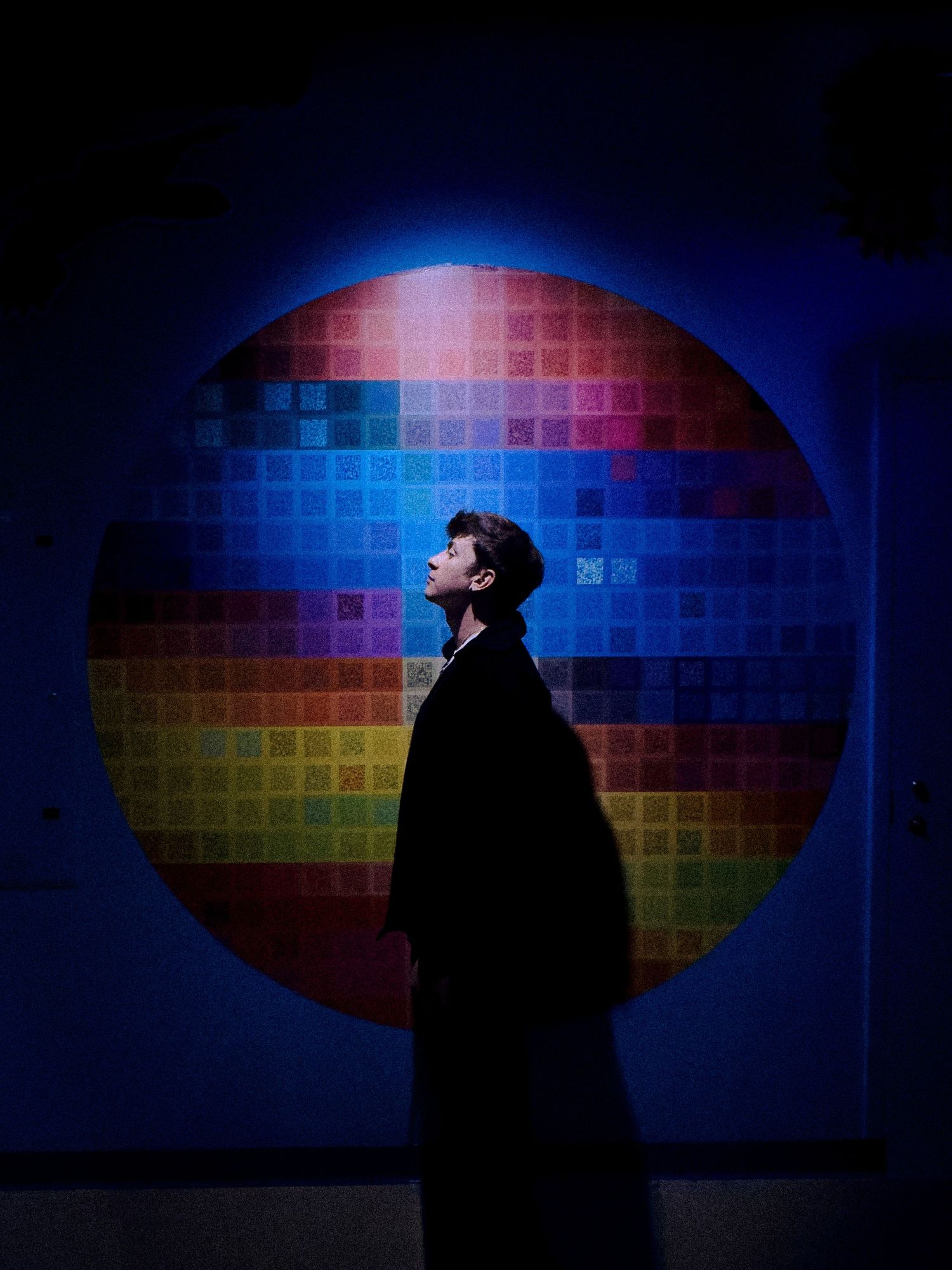 Artistic silhouette against colorful geometric light wall display.