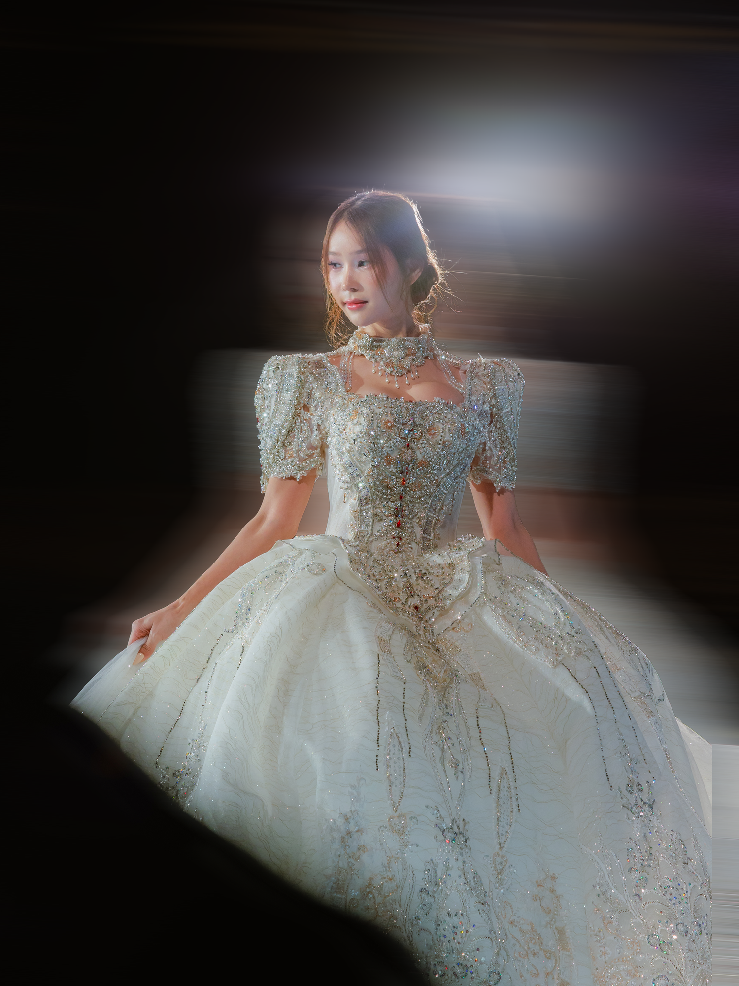 Ethereal white ball gown with intricate gold embellishments and puff sleeves photographed in dramatic lighting.