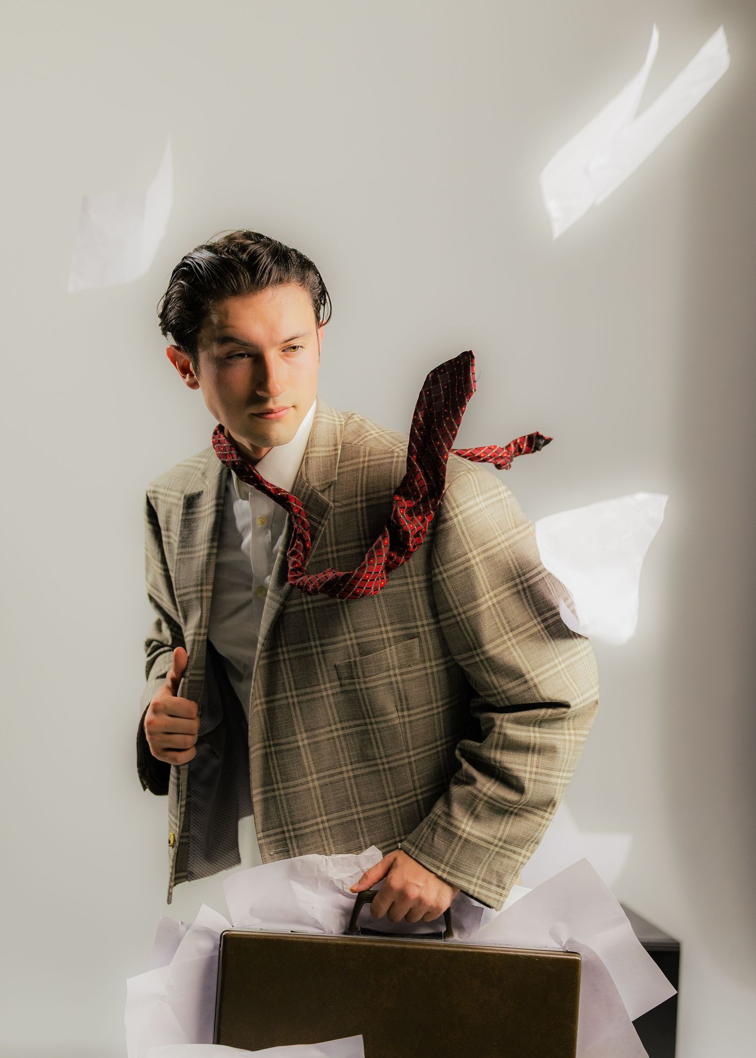 Person in plaid blazer posing against white wall with dramatic lighting.