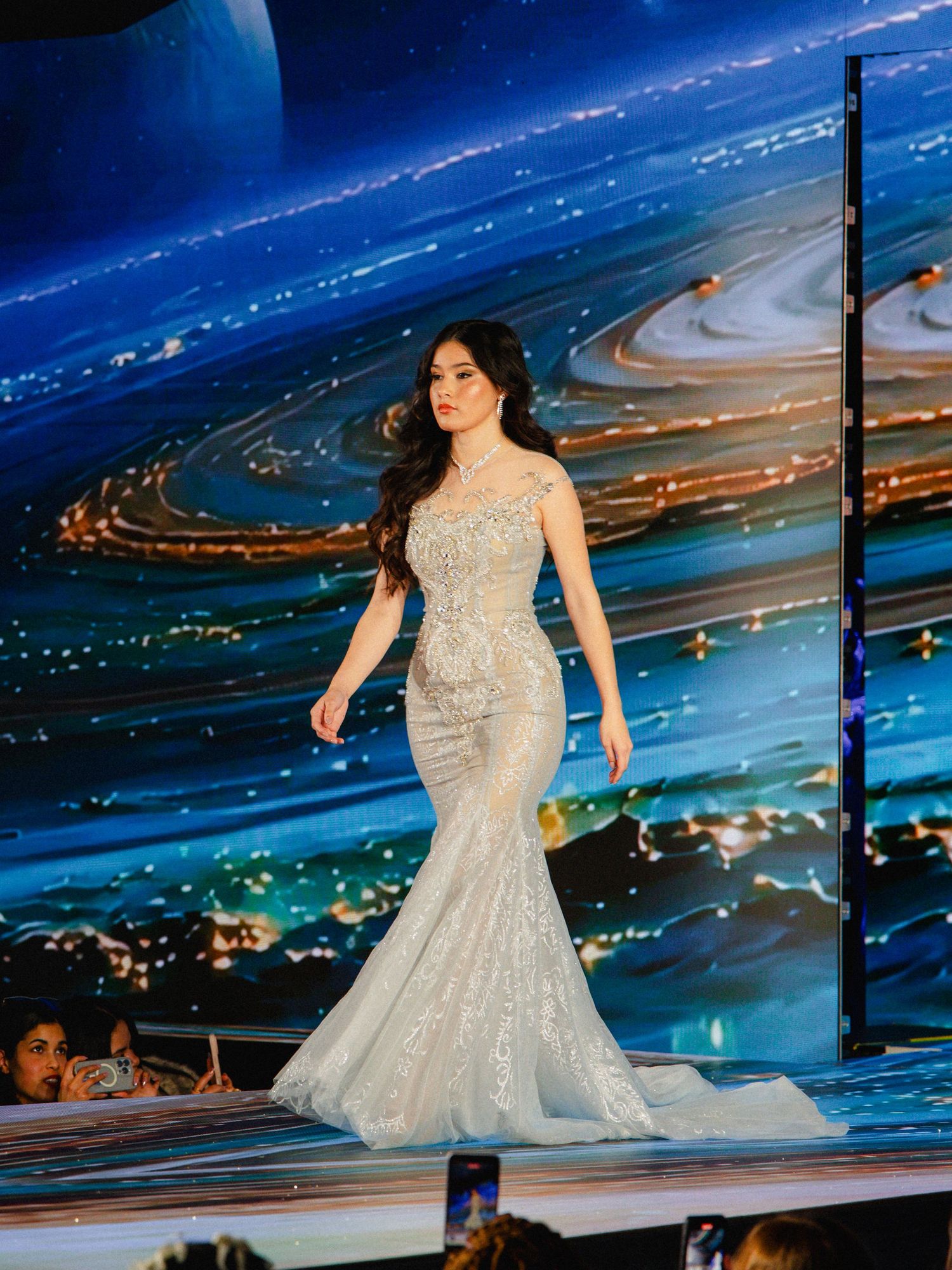 A sparkling white ballgown dress with intricate beading reflects against dramatic blue lighting on a stage.
