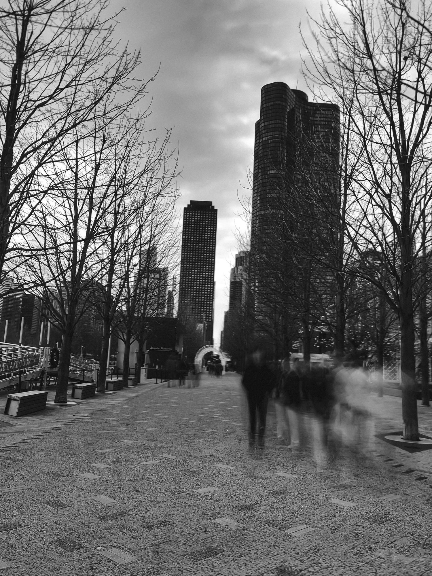 Black and white cityscape with blurred figures walking near urban buildings.