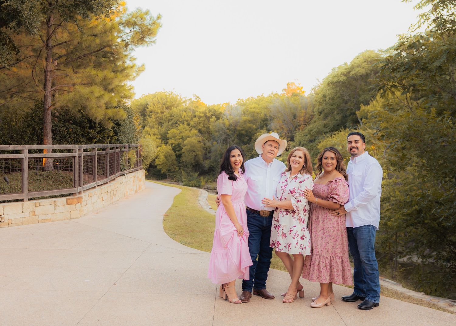 Family members in coordinating pink and white outfits pose for outdoor portraits at sunset.