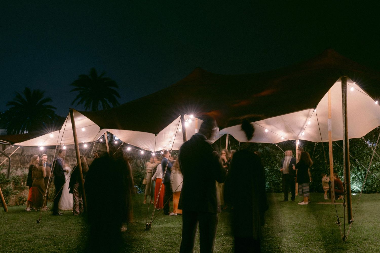 Wedding guests mingling under tents during evening wedding reception