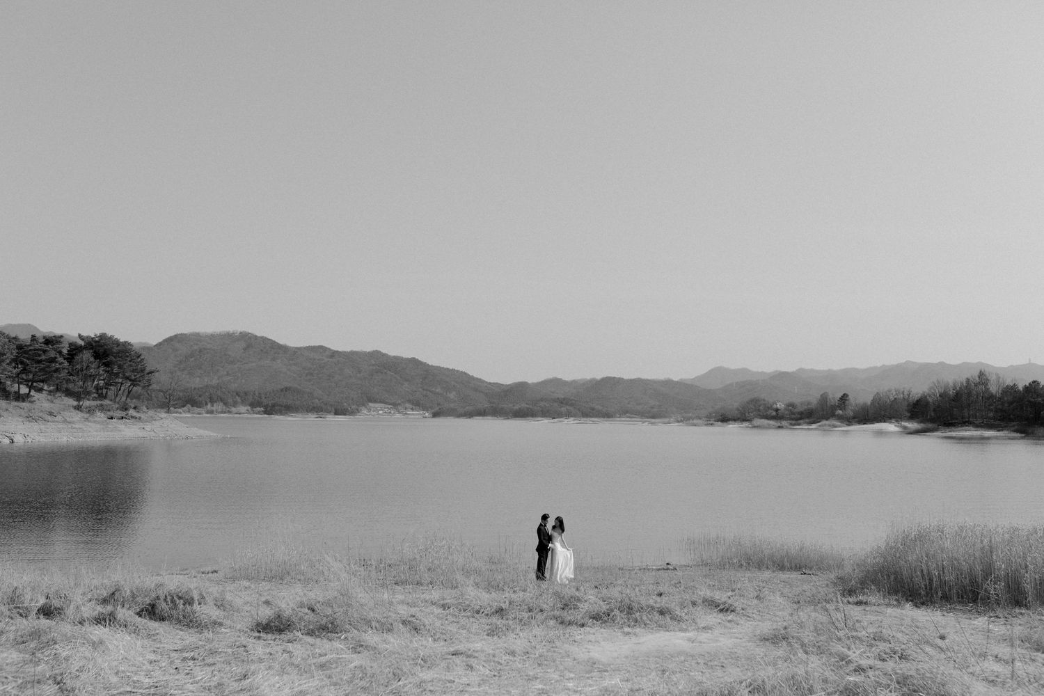Couple embracing by lake with mountain backdrop during wedding in South Korea