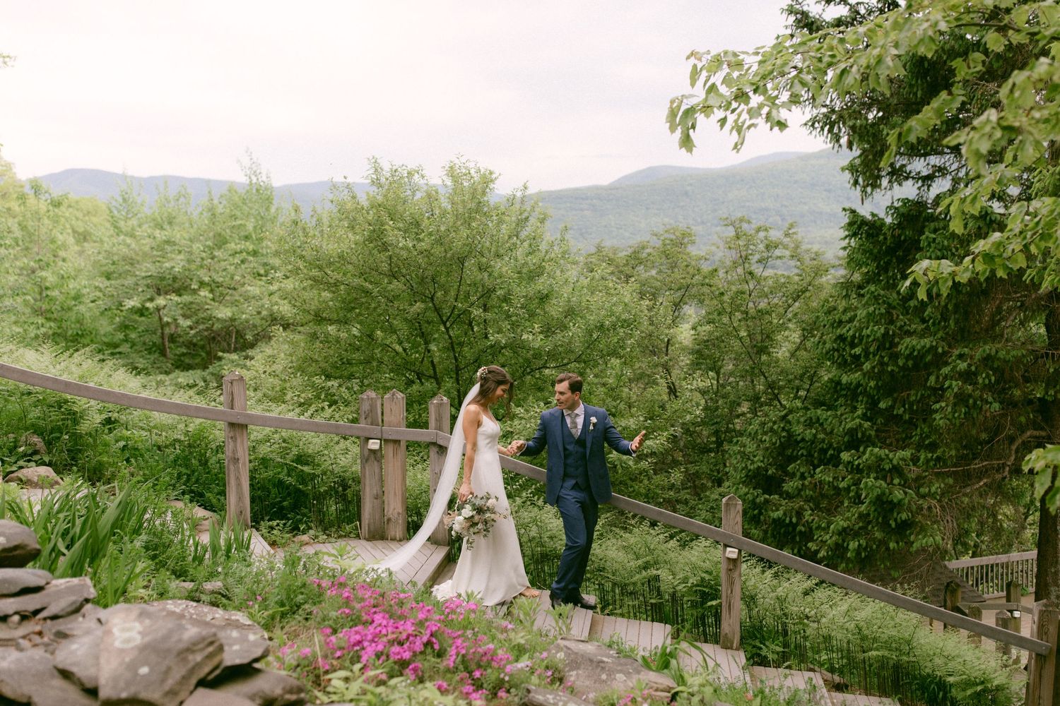 Bride and groom walking hand in hand along wooden fence surrounded by mountain scenery at Onteora Mountain House in the Catskills, New York