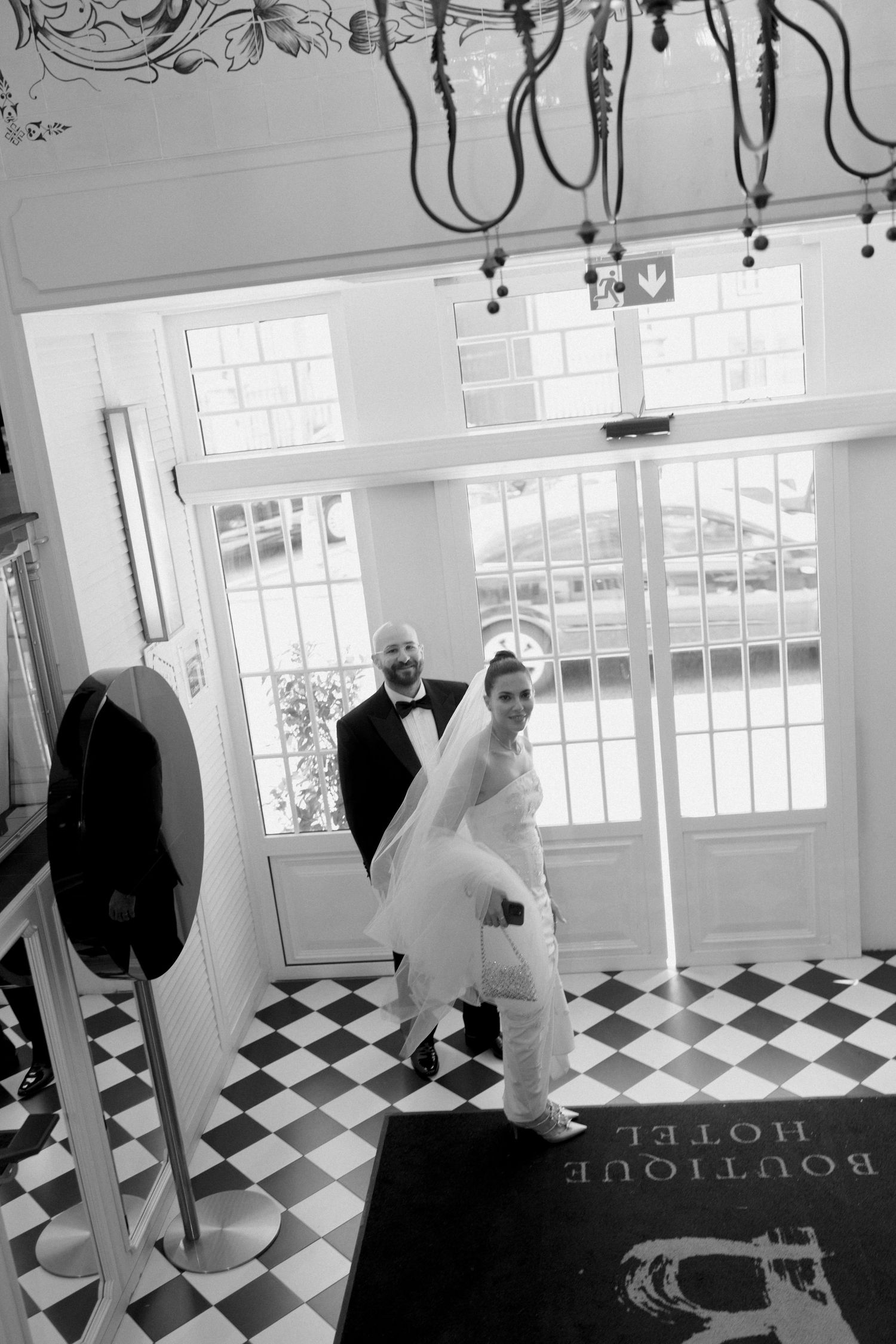 Black and white photo of bride and groom entering boutique hotel with checkered floor