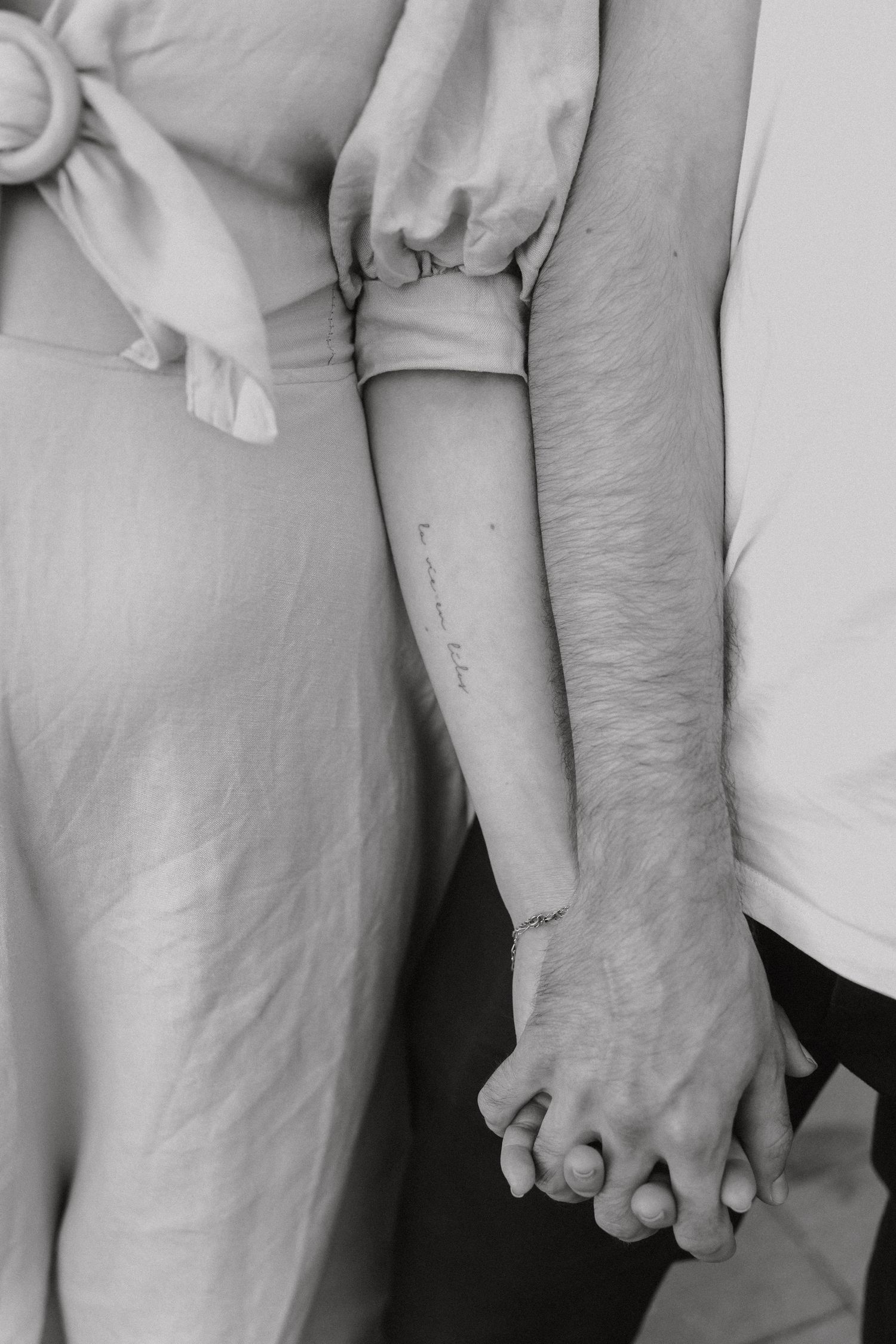 Close-up of couple holding hands, woman wearing linen dress with forearm tattoo