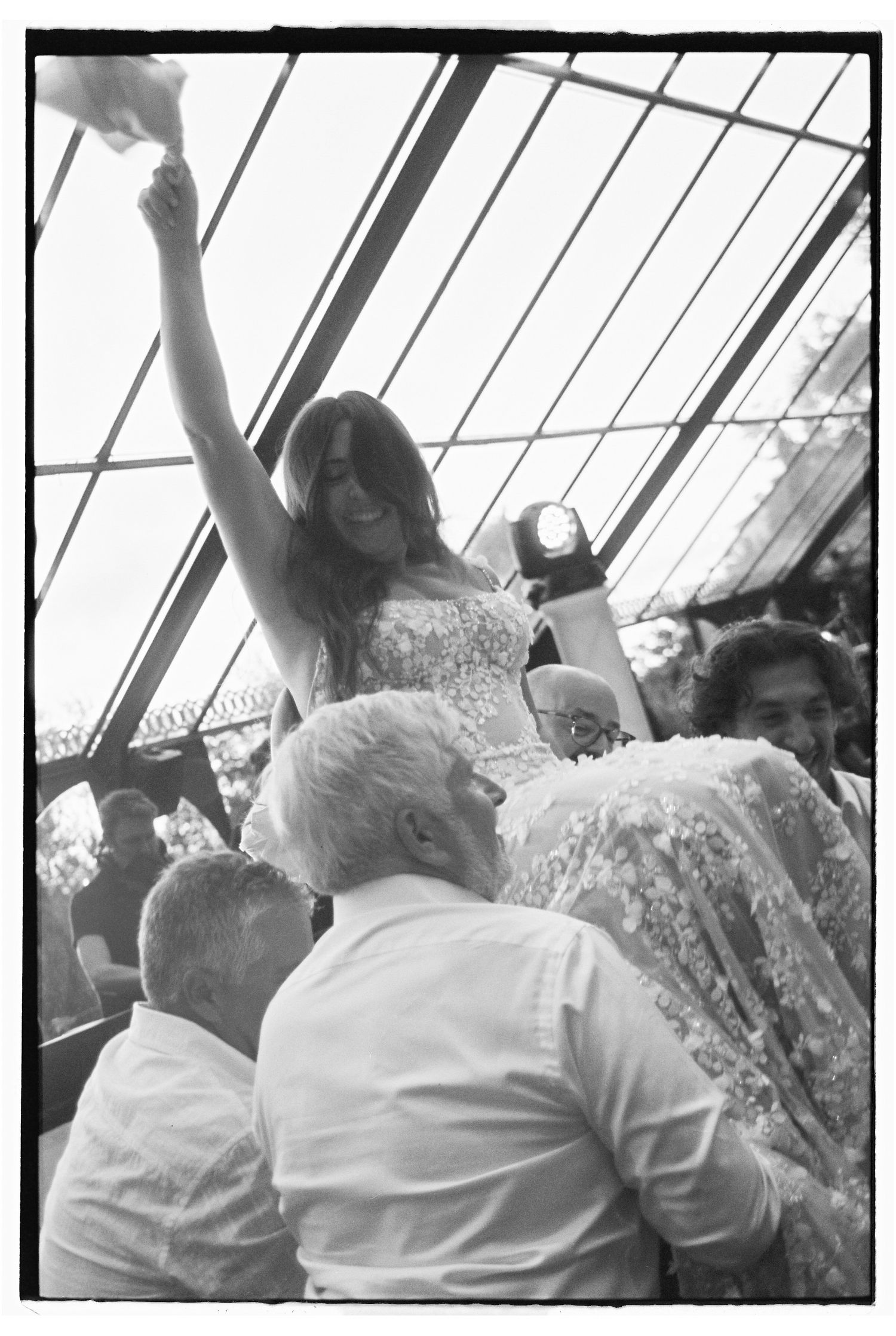 Bride in lace gown lifted by guests during hora at Jewish wedding reception