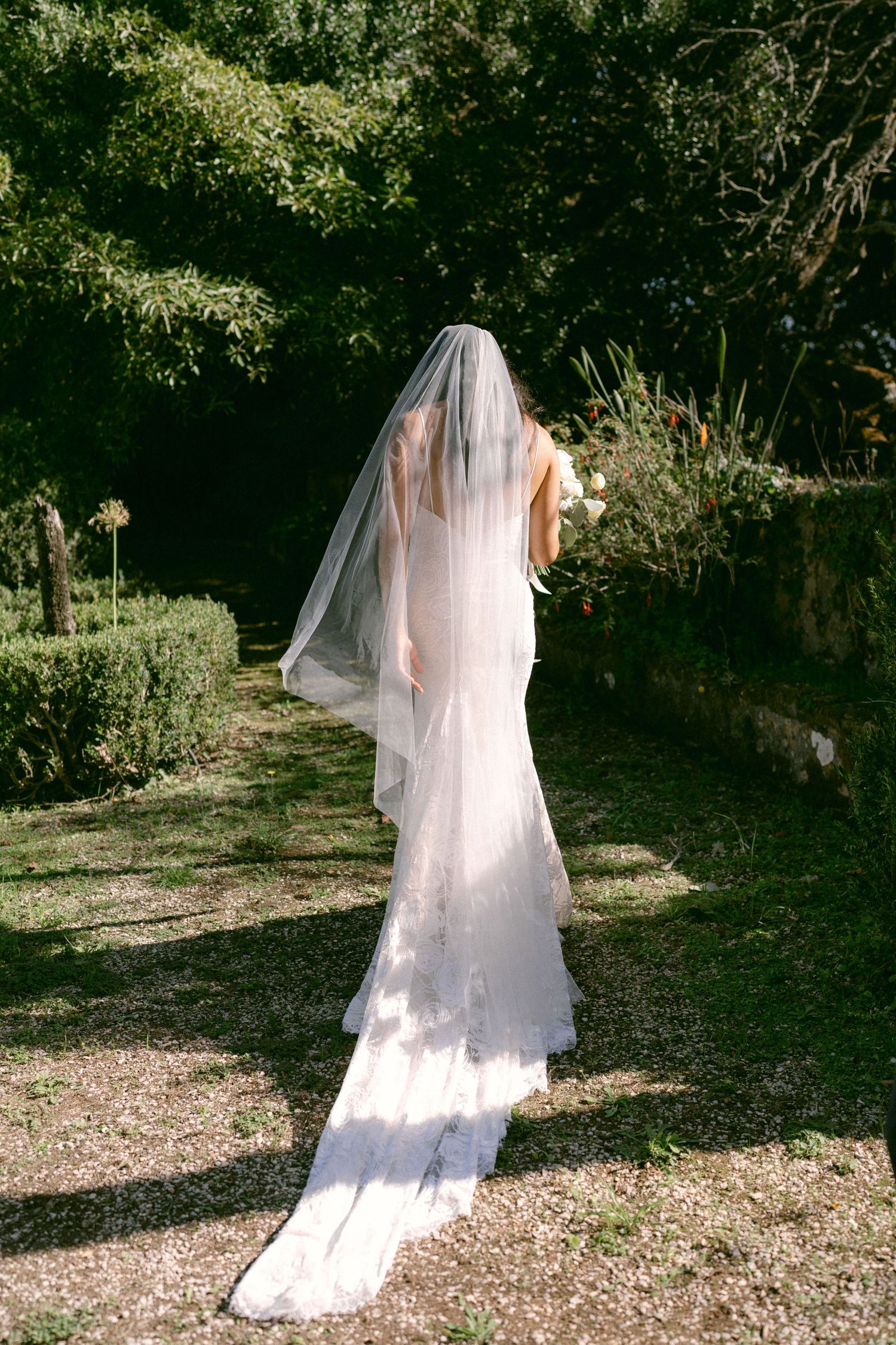 Bride walking through garden path in wedding dress during outdoor ceremony