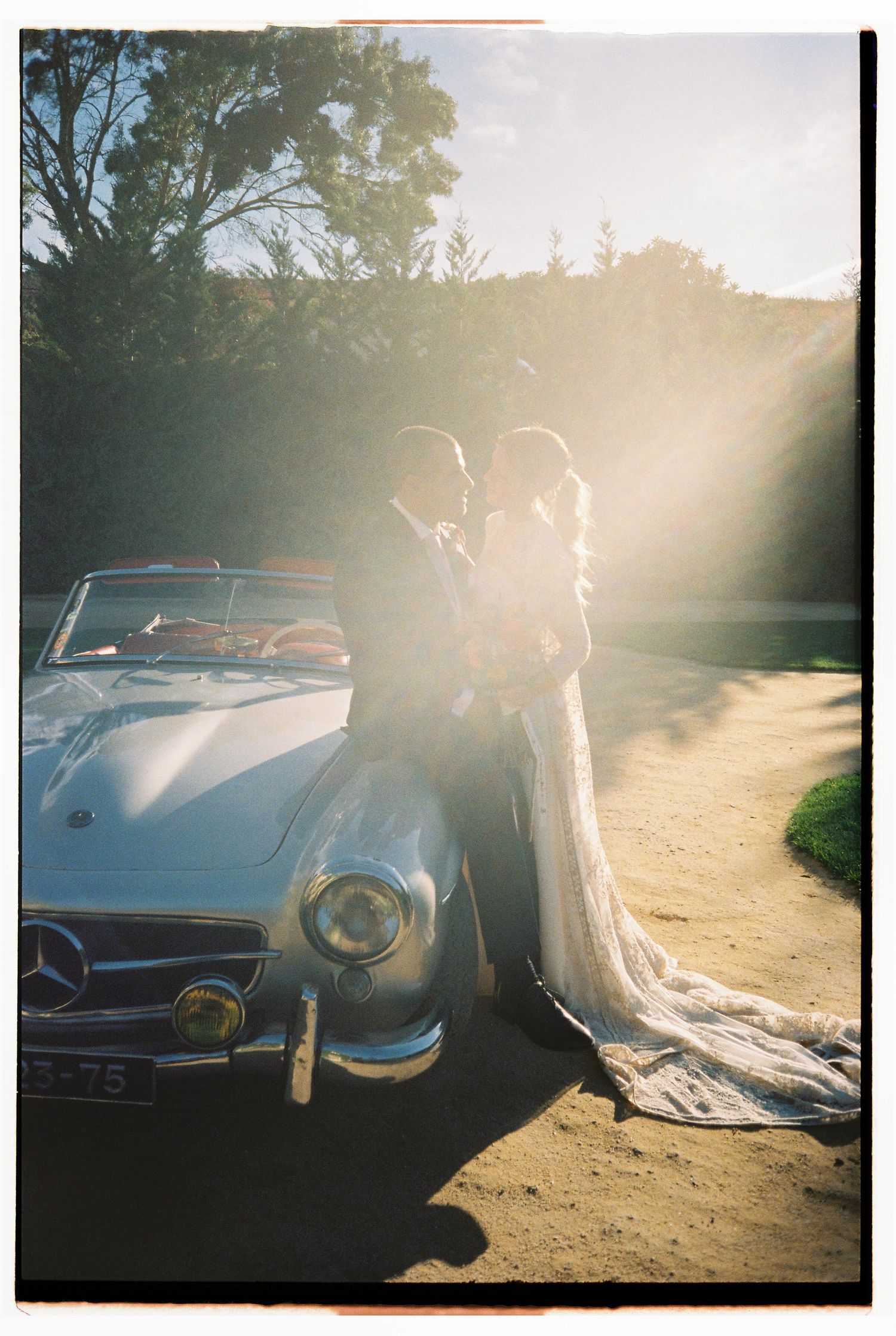 Bride and groom embracing beside vintage Mercedes convertible at sunset during wedding