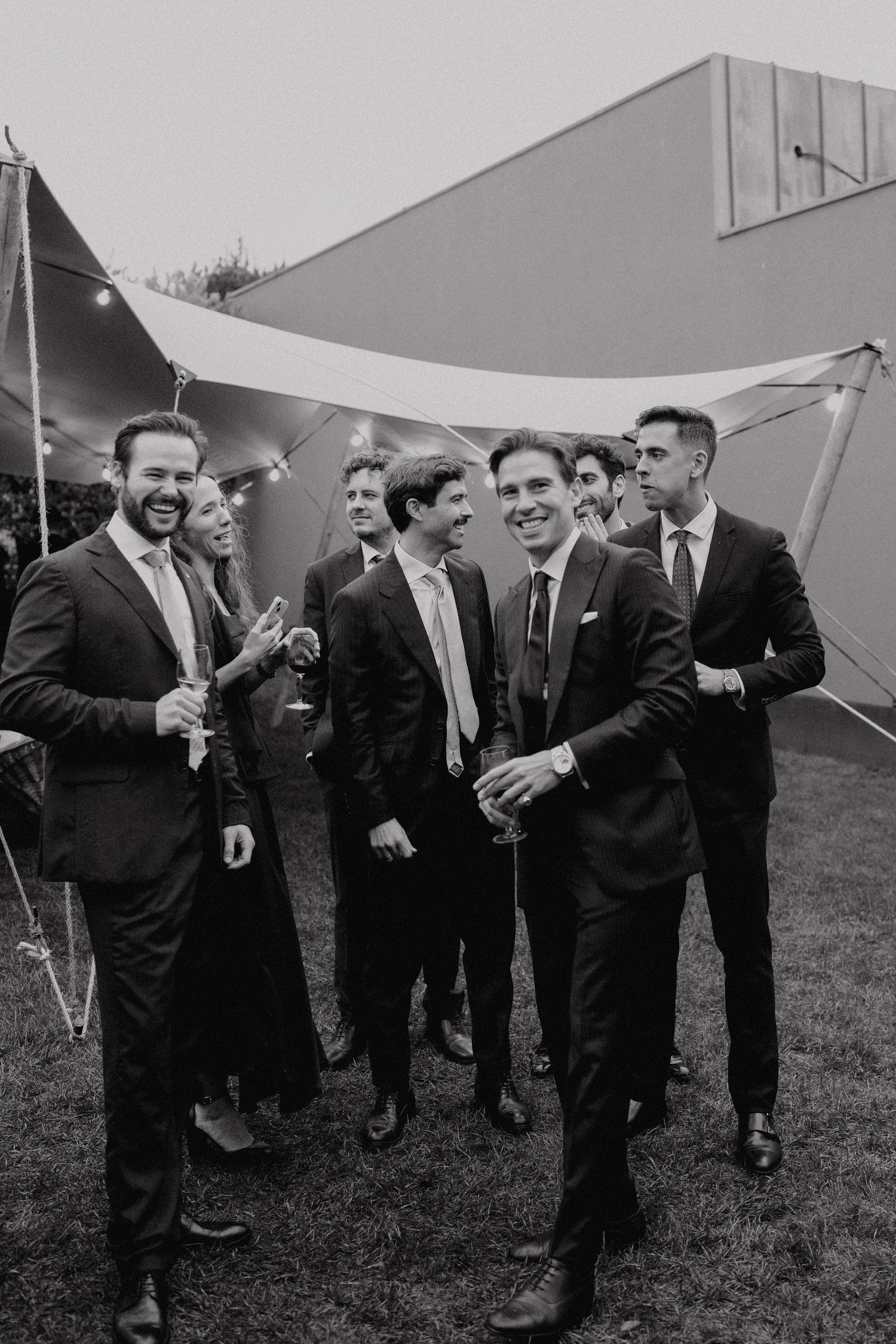 Groomsmen and wedding guests laughing together outdoors during wedding reception