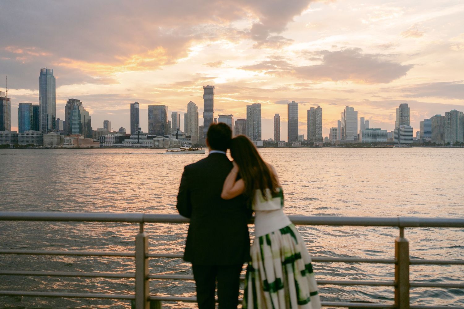 Couple embracing while watching sunset over city skyline from waterfront promenade in New York City