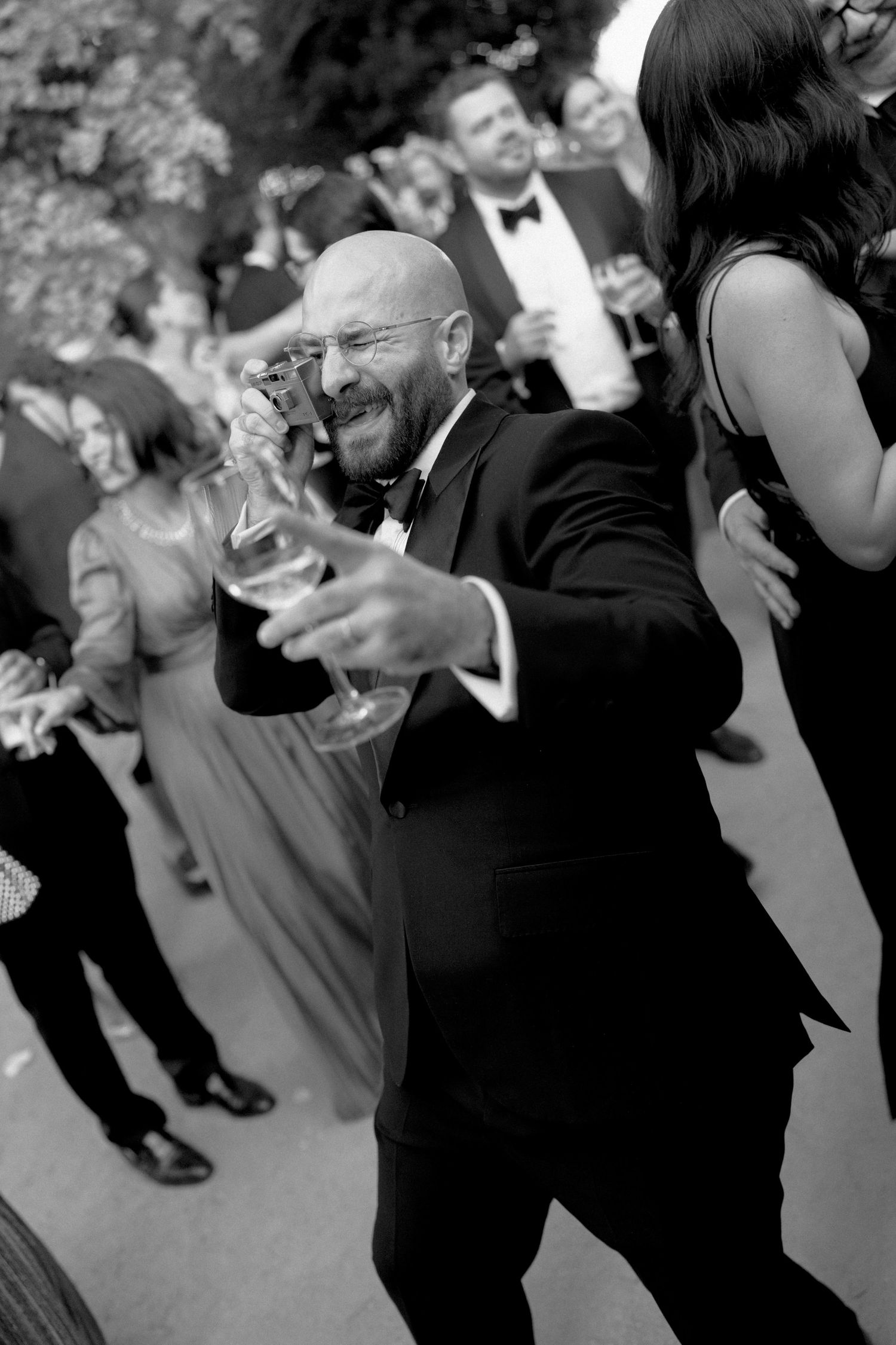 Groom dancing while taking photo with camera and holding champagne during wedding reception