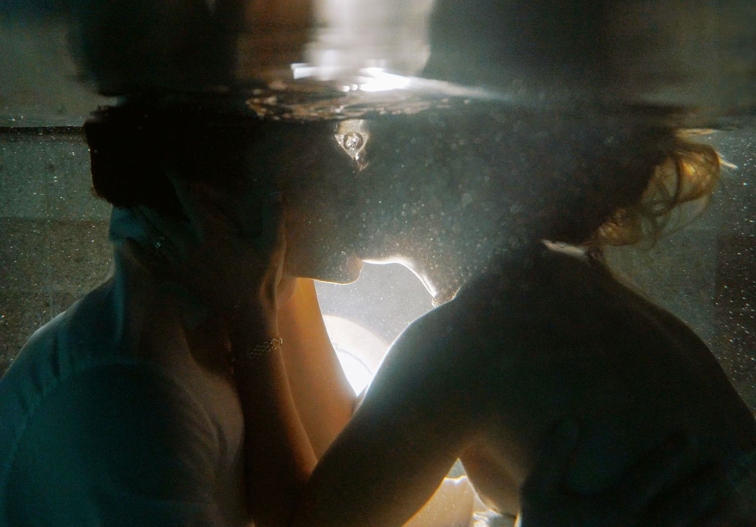 Bride and groom kissing underwater in pool with light filtering through the water